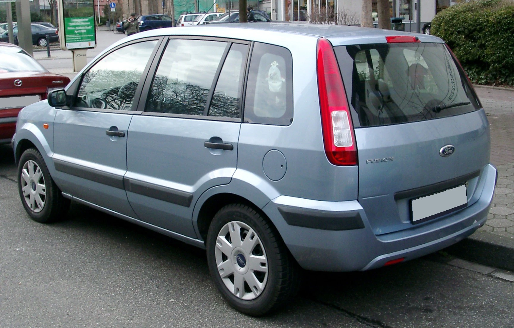 Silberner Kompaktwagen, geparkt am Straßenrand. Fünf Türen, modernes Design, umgeben von anderen Autos und städtischer Umgebung.