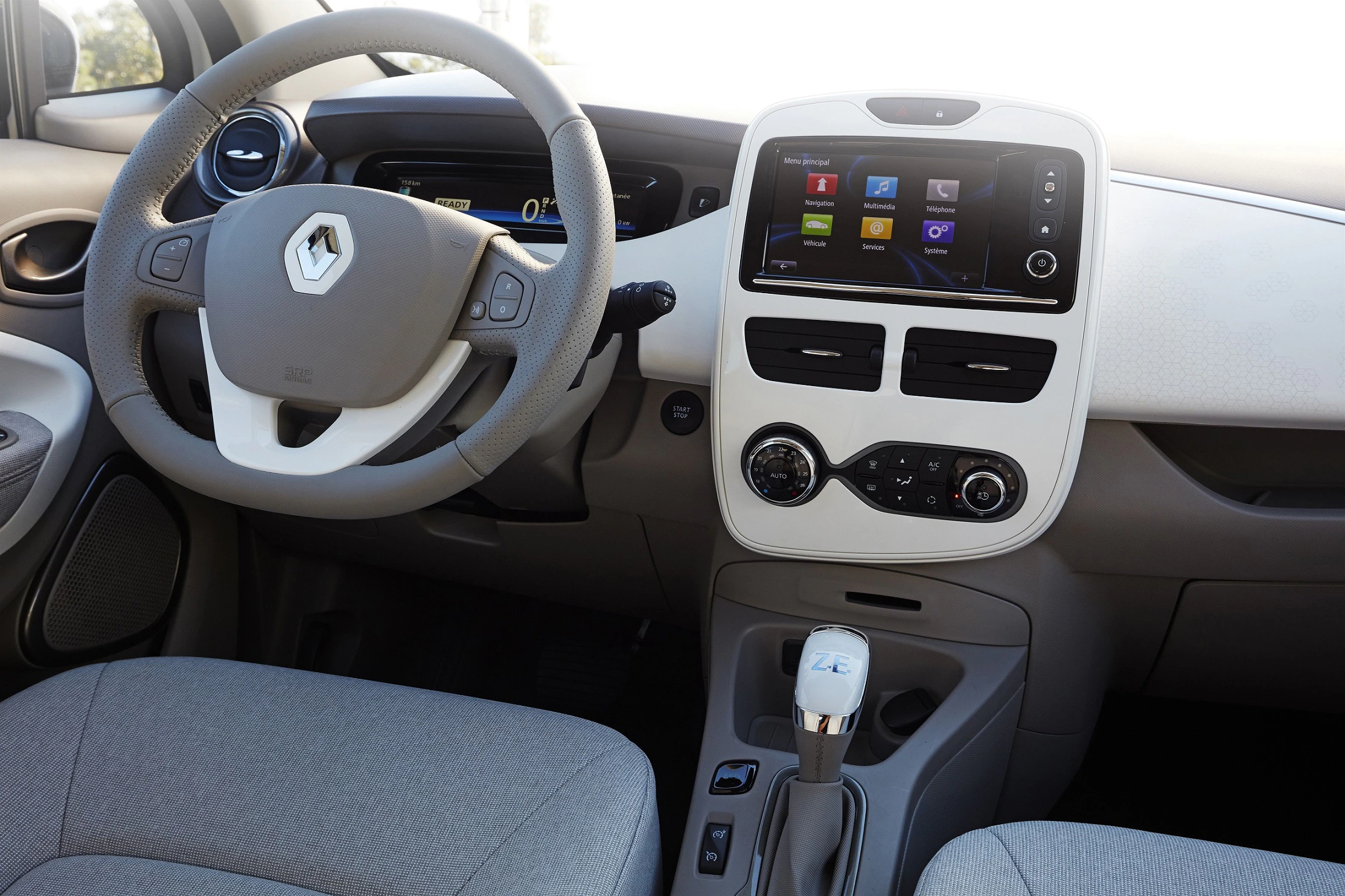 Innenraum eines Renault mit Lenkrad, Infotainment-Bildschirm und Schalthebel. Helle Sitze, modern gestaltetes Armaturenbrett.