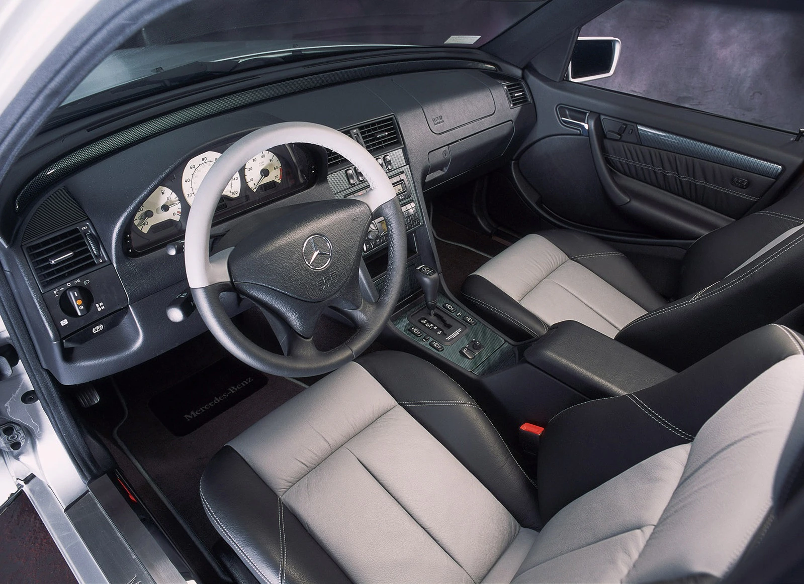 Innenraum eines Mercedes-Benz mit grauen Ledersitzen, schwarzem Armaturenbrett und Steuer, Schaltknüppel und modernem Cockpit.