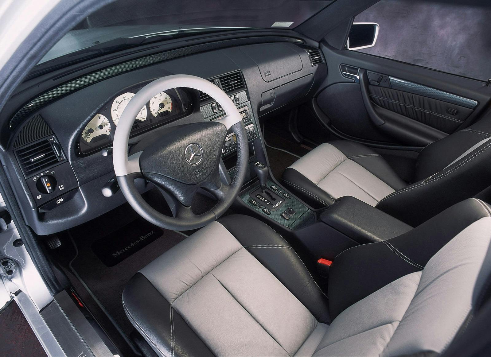 Innenraum eines Mercedes-Benz mit grauen Ledersitzen, schwarzem Armaturenbrett und Steuer, Schaltknüppel und modernem Cockpit.