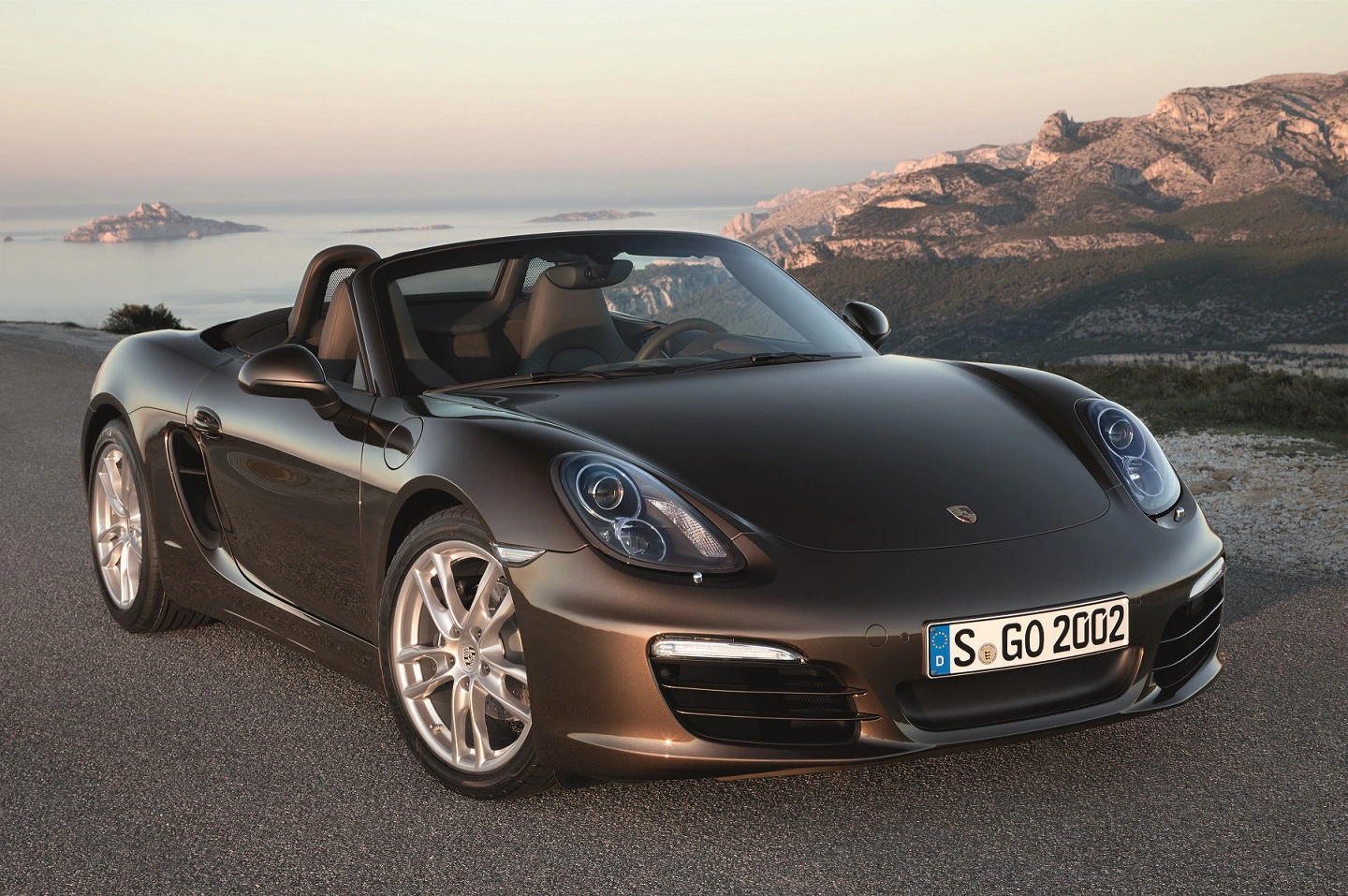 Schwarzer Sportwagen (Cabrio) auf einer Straße, im Hintergrund eine Berglandschaft bei Sonnenuntergang.