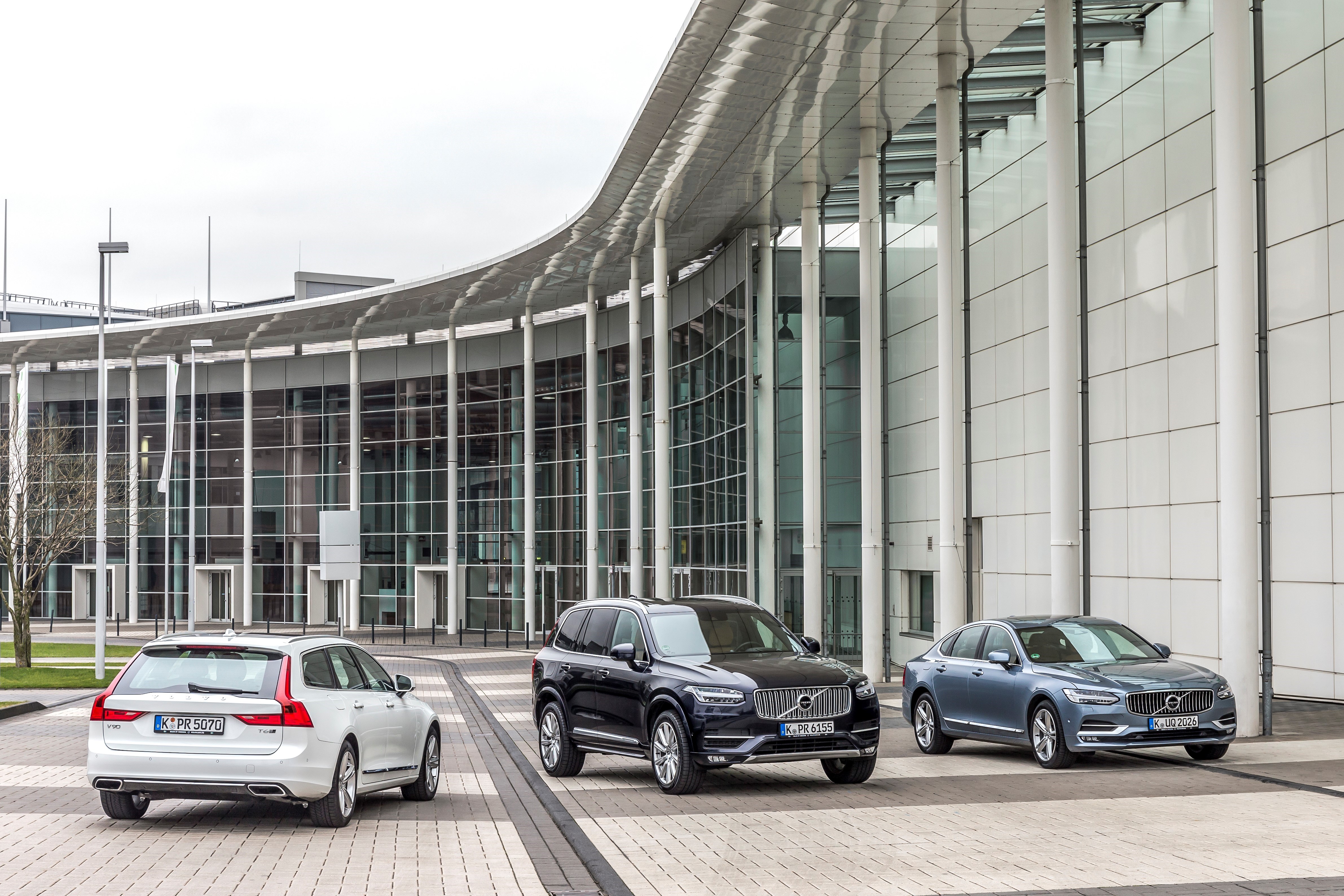 Drei Volvo-Modelle sind vor einem modernen Gebäude mit Glasfassade geparkt. Sie stehen in einer stilvollen, urbanen Umgebung.