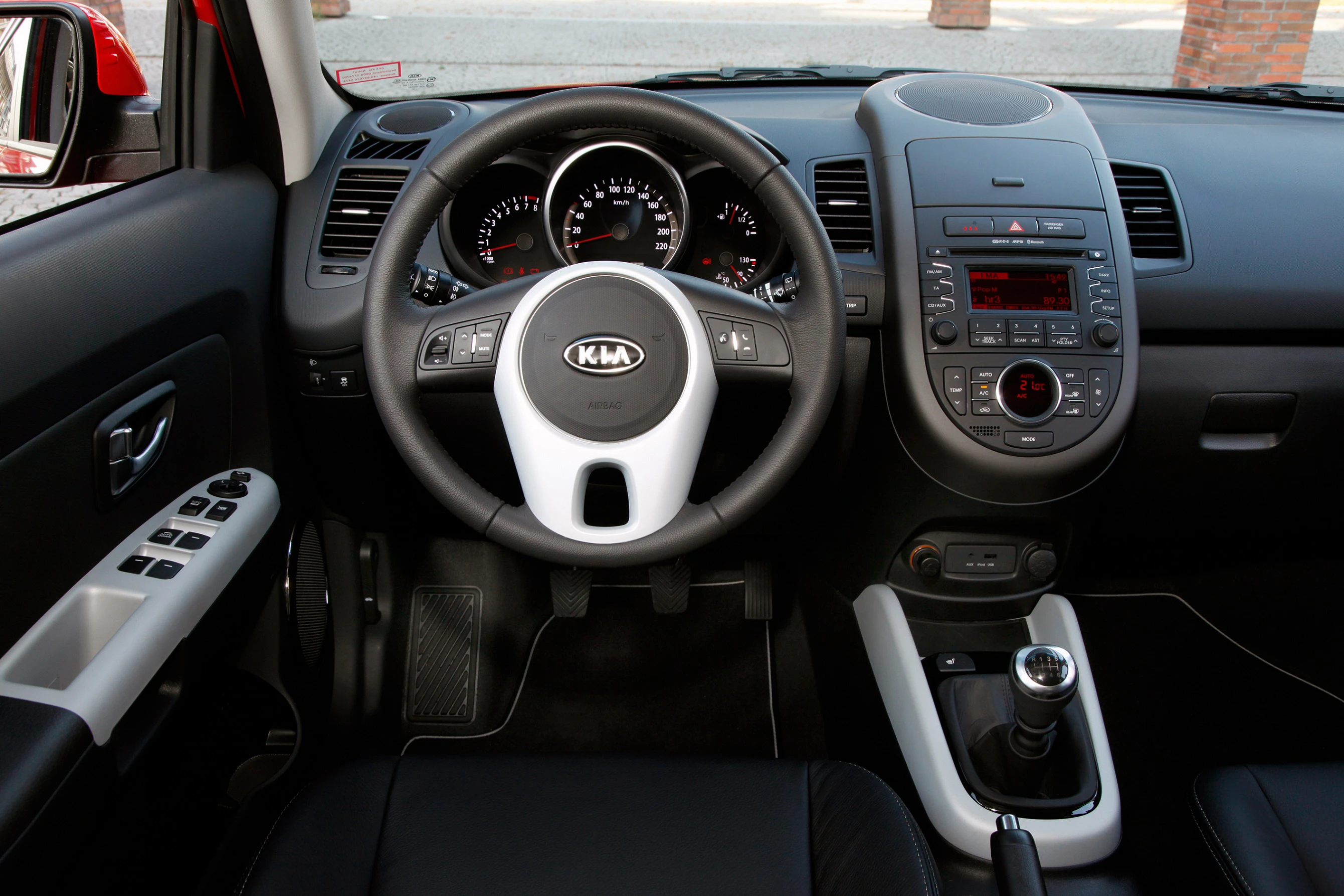 Innenraum eines Autos mit Lenkrad, Armaturenbrett, Schalthebel und mehreren Bedienelementen. Moderne Gestaltung mit schwarzem Interieur.