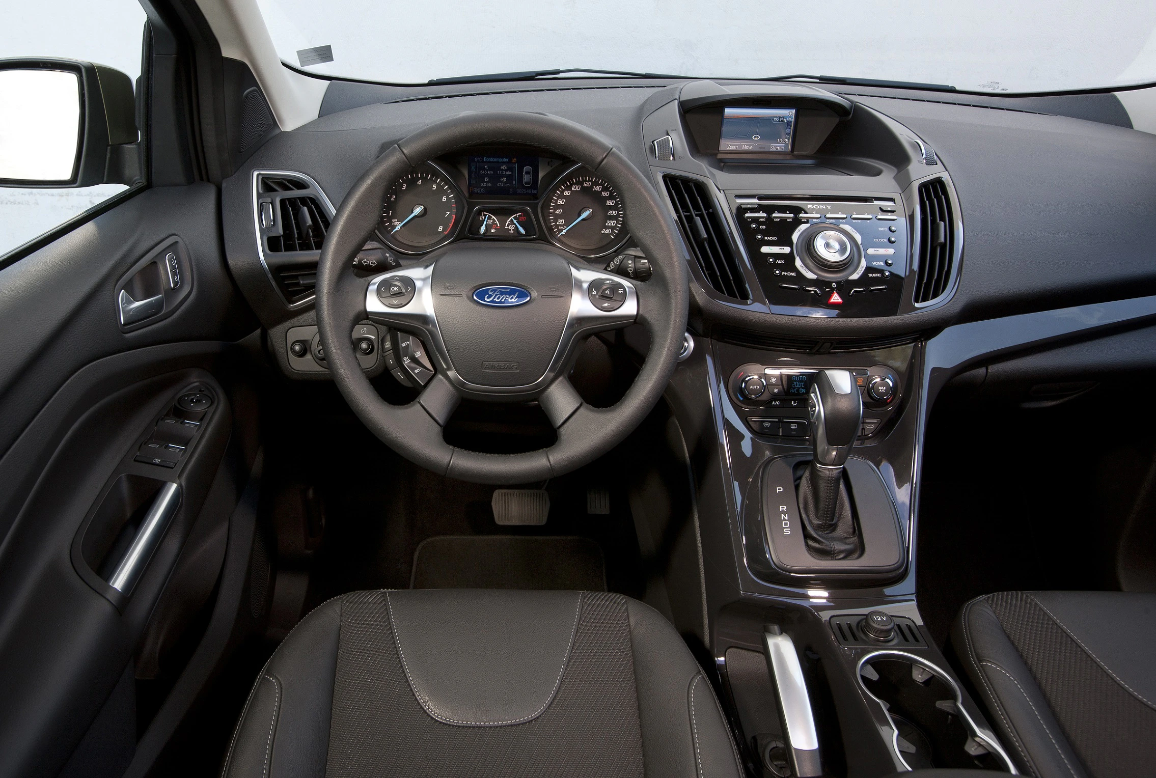 Lenkrad und Armaturenbrett eines modernen Autos mit Ford-Logo, Anzeigen und Steuerungselementen in einem schwarzen Innenraum.