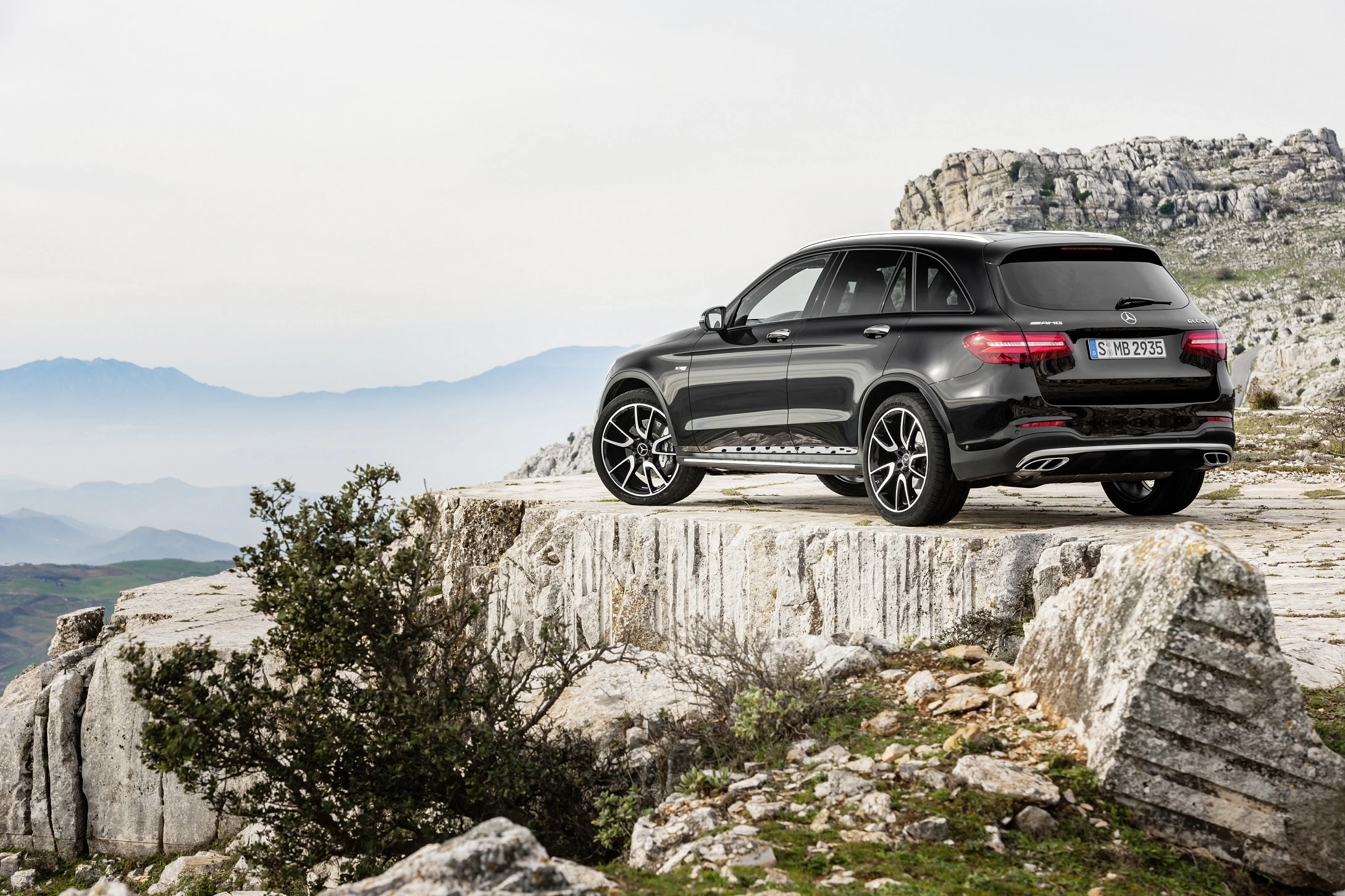 Schwarzer SUV auf felsigem Plateau mit Bergblick und nebligem Himmel im Hintergrund.
