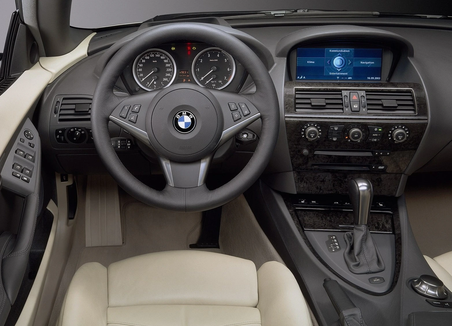 Innenraum eines BMW mit Lederlenkrad, Tachometern und Navigationsdisplay. Beigefarbene Ledersitze und Mittelkonsole sind sichtbar.