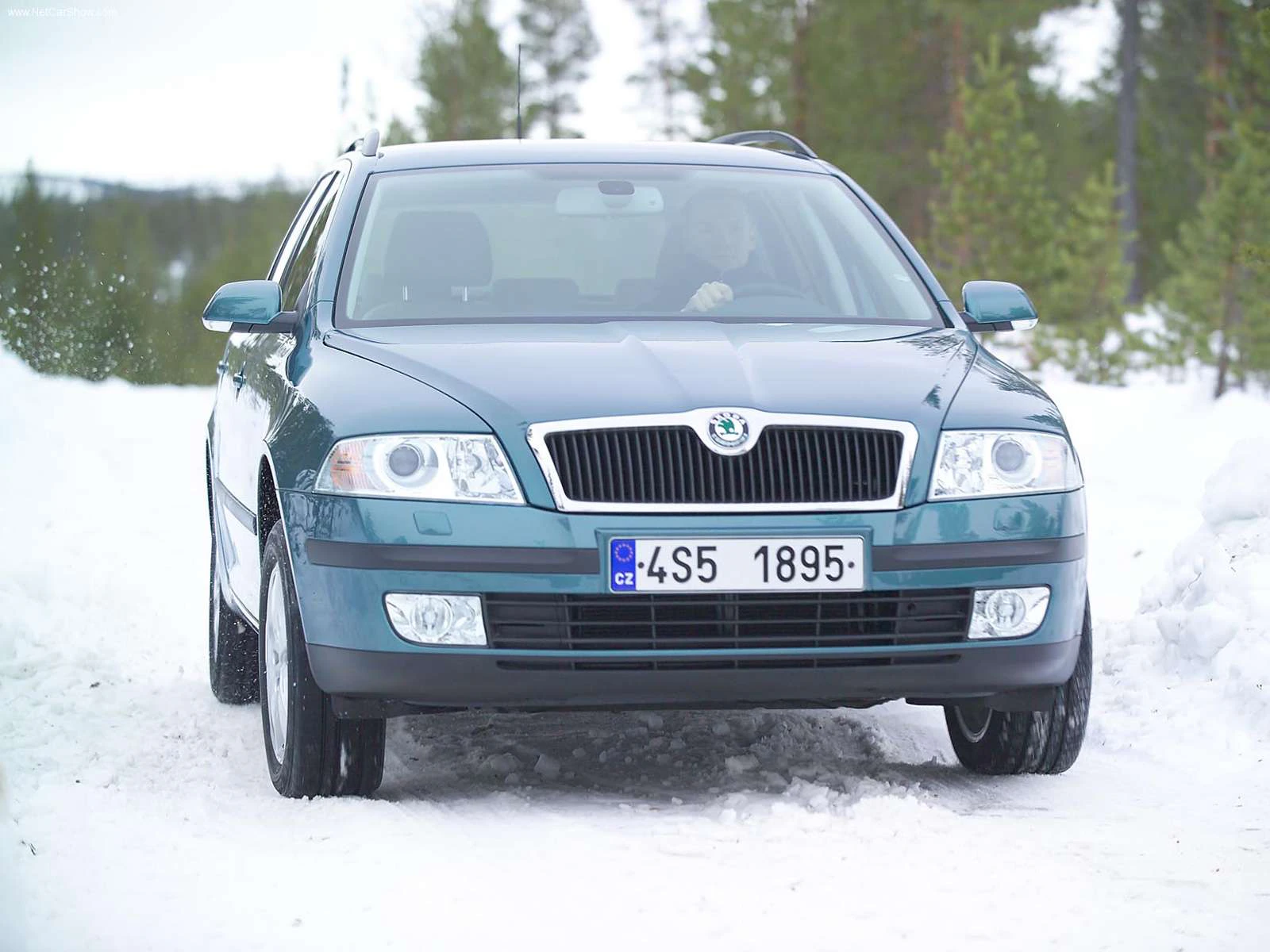 Skoda-Auto auf schneebedeckter Straße in winterlicher Landschaft, mit Schnee auf den Seiten und Kiefern im Hintergrund.