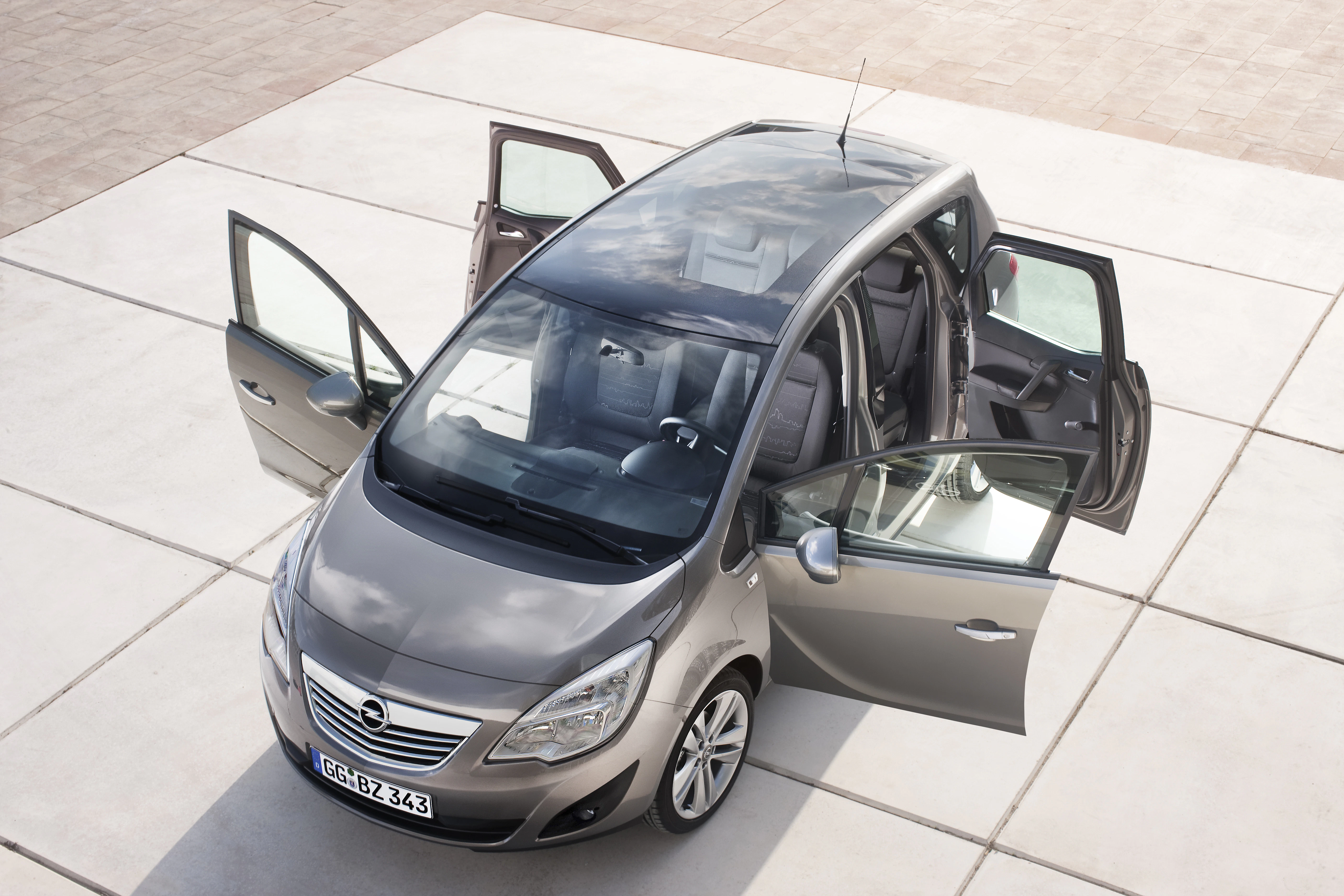 Silberner Opel Meriva mit allen geöffneten Türen, von oben fotografiert, auf hellem Pflaster geparkt.
