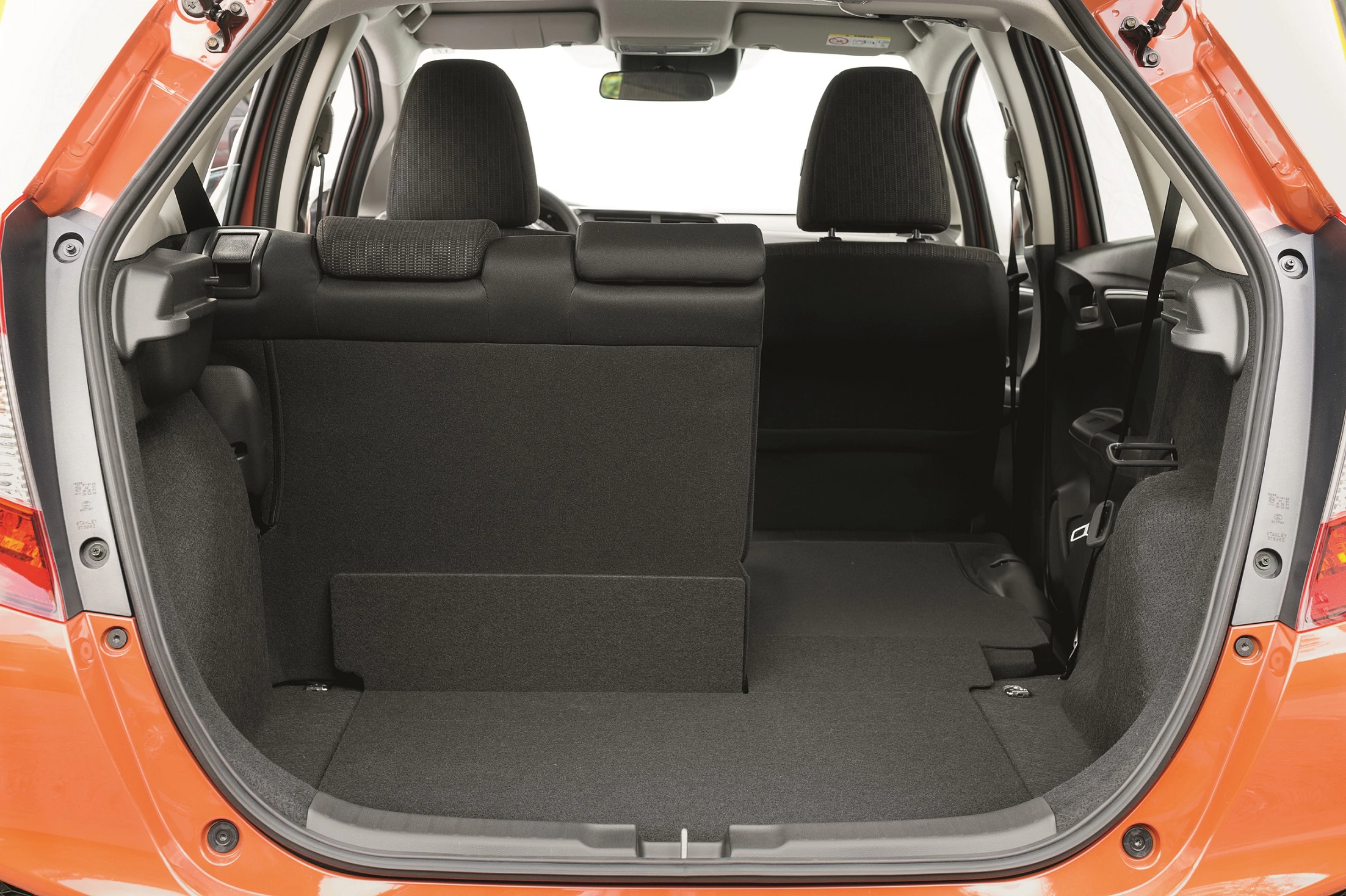 Innenansicht eines offenen Kofferraums eines orangefarbenen Autos mit klappbarer Rückbank und schwarzem Stoffbezug.