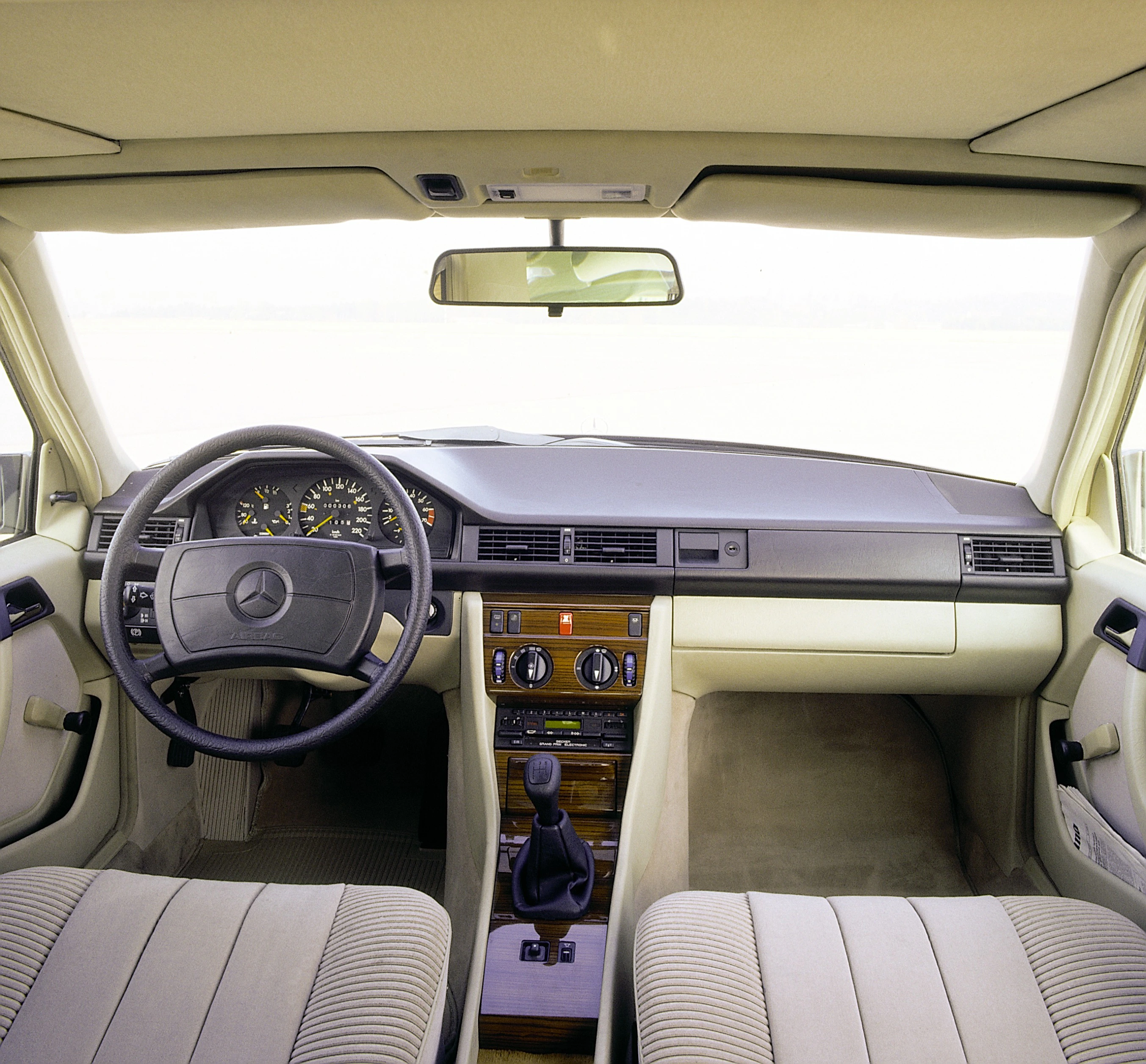 Innenraum eines klassischen Mercedes-Benz mit Armaturenbrett, Lenkrad, Gangschaltung und beigen Sitzen. Ansicht von hinten nach vorn.