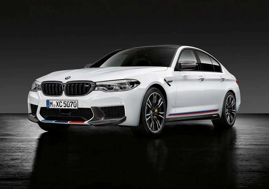Weißer BMW M5 mit sportlichem Design und blauen Akzenten, seitlich fotografiert auf dunklem Hintergrund.