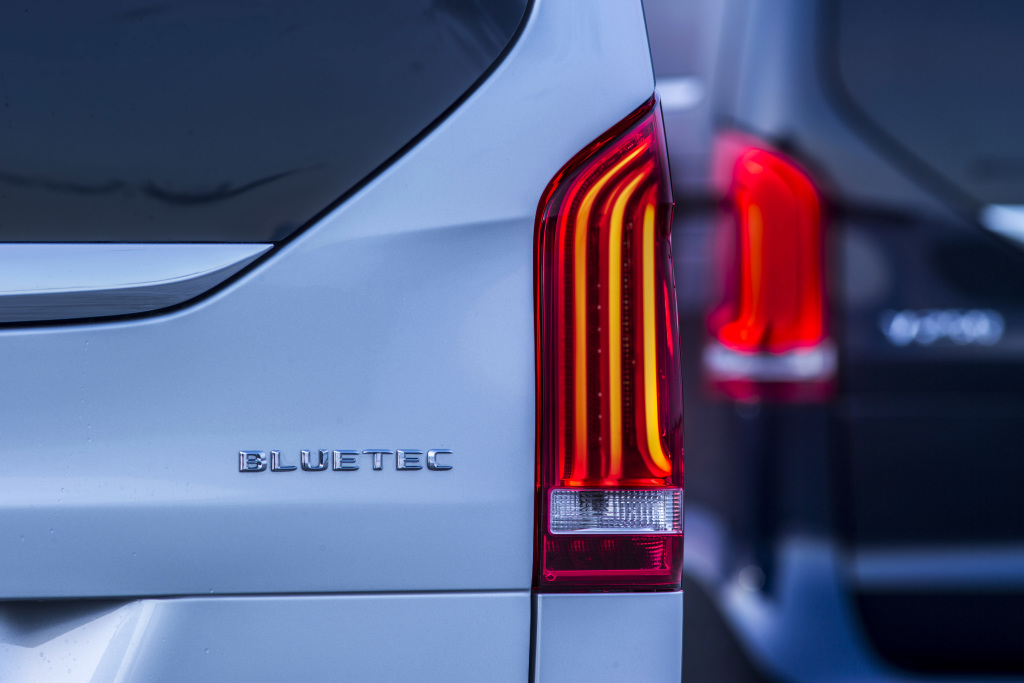 Nahaufnahme von zwei Autos, Fokus auf den markanten roten Rücklichtern eines weißen Fahrzeugs mit dem "Bluetec"-Emblem.