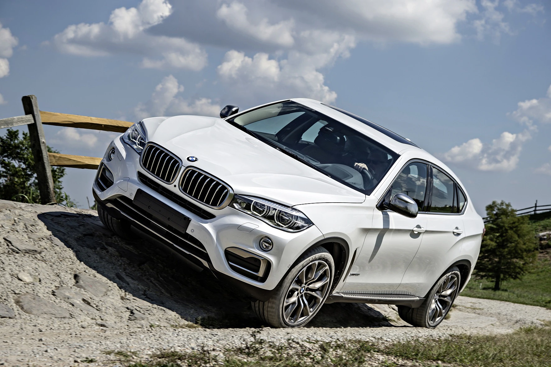 Weiße Mittelklasse-SUV fährt bergauf auf steinigem Gelände, mit blauem Himmel und Wolken im Hintergrund.