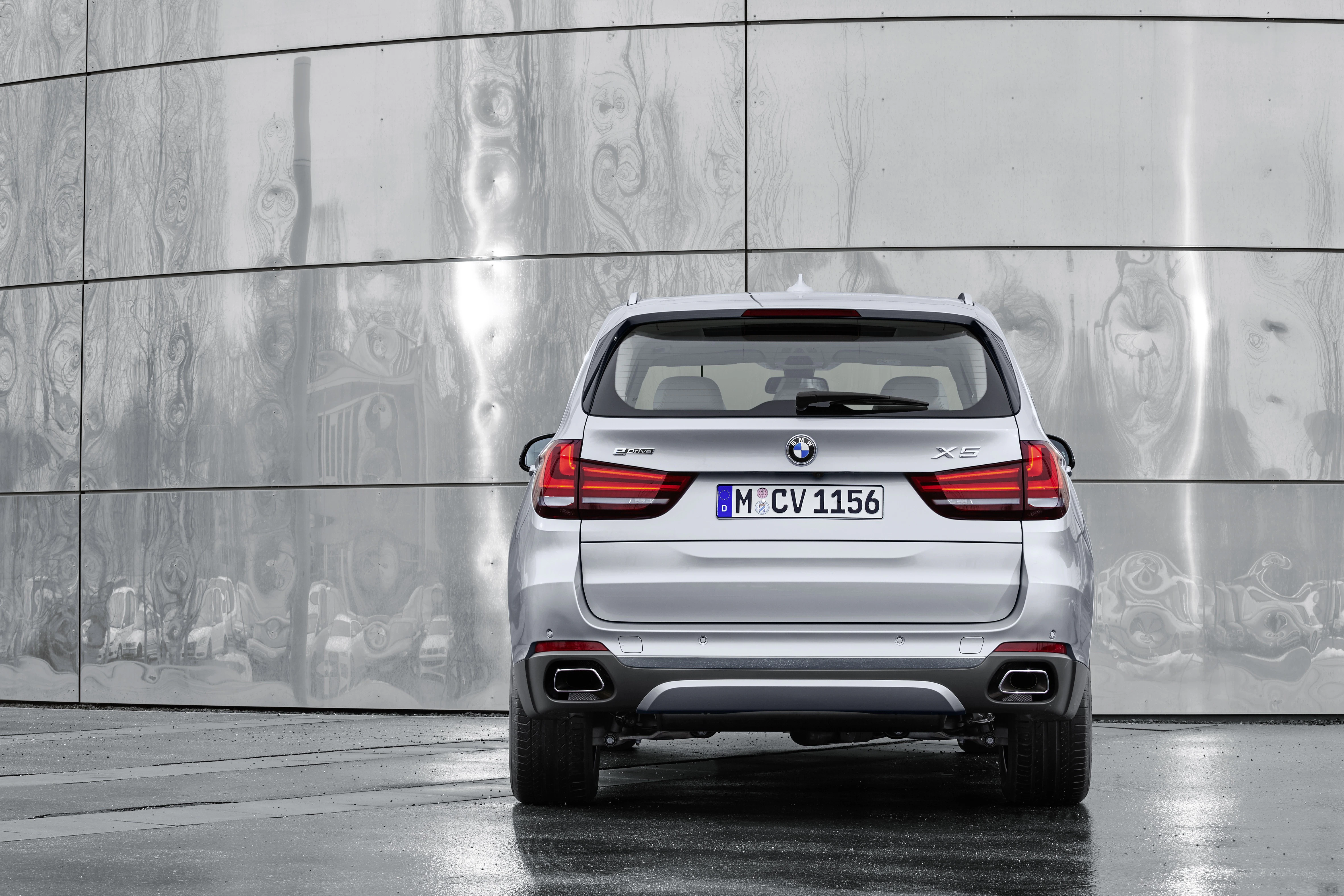 Silberner BMW X5-SUV vor einer modernen, metallischen Fassade geparkt. Rückansicht des Fahrzeugs.