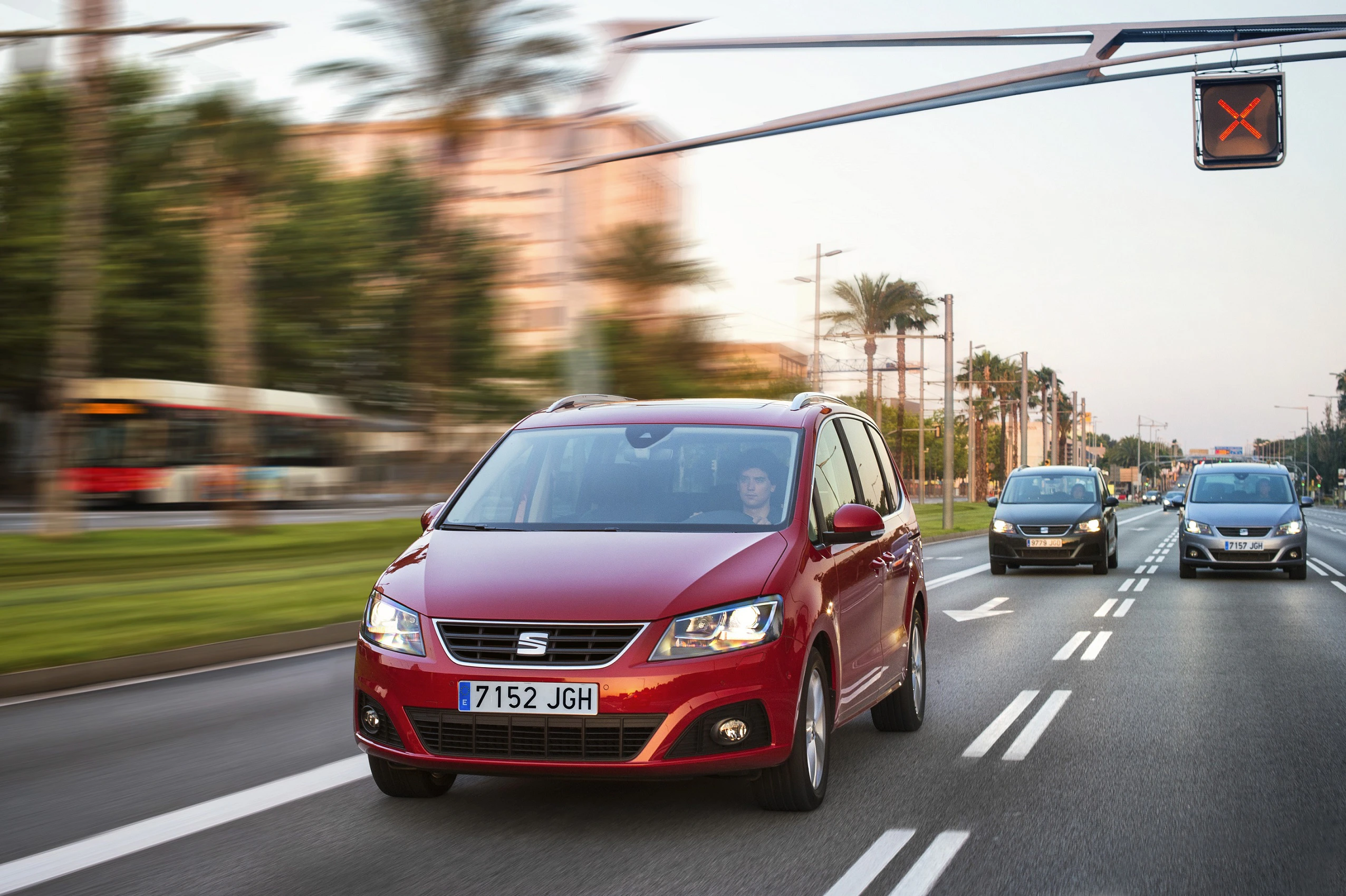 Roter Seat Alhambra fährt auf einer mehrspurigen Straße bei Ampellicht, umgeben von anderen Autos und Palmen im Hintergrund.