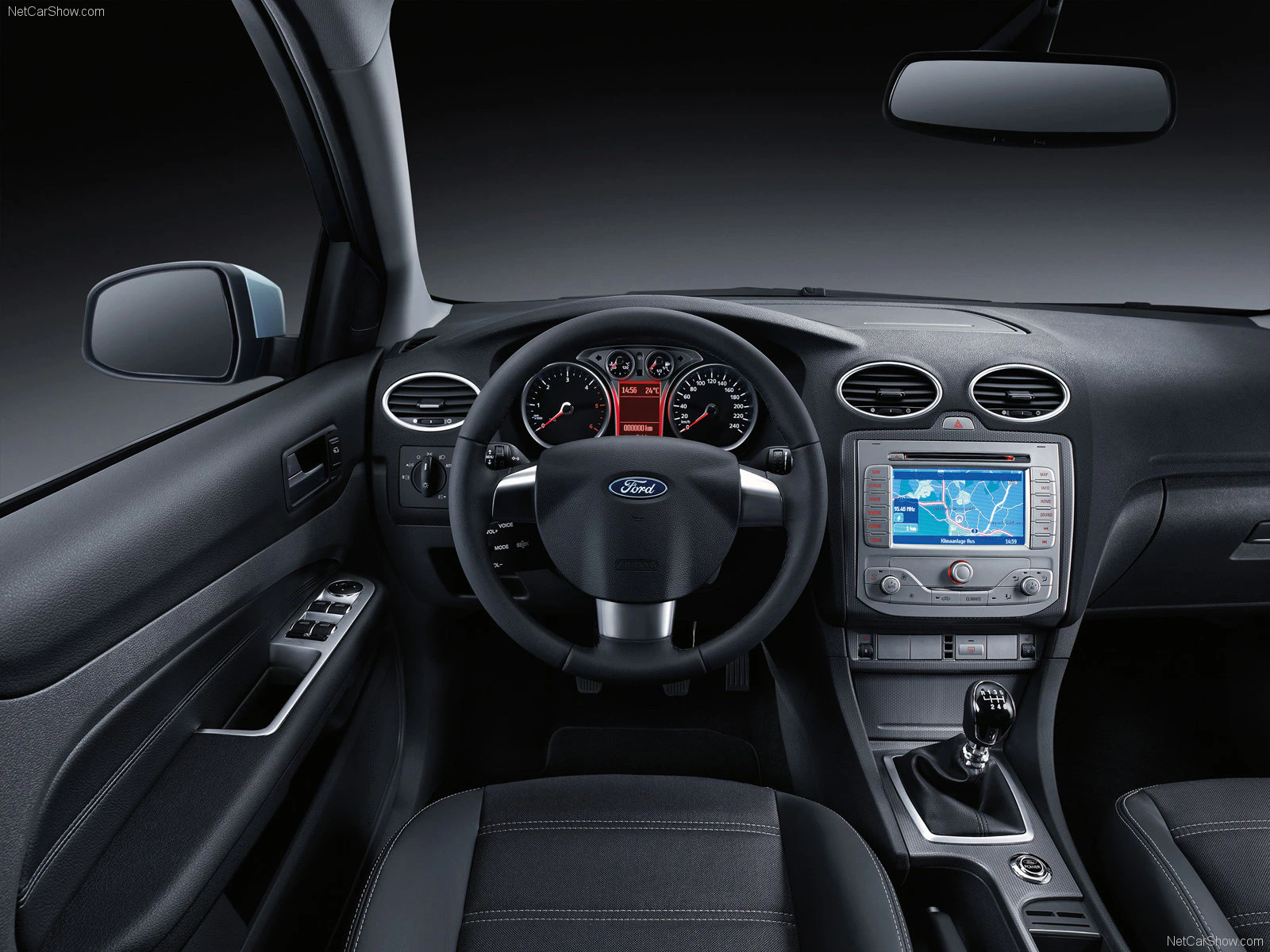 Innenraum eines Autos mit Lenkrad, Tachometer, Bildschirm mit Navigation, Schalthebel und schwarzen Ledersitzen.