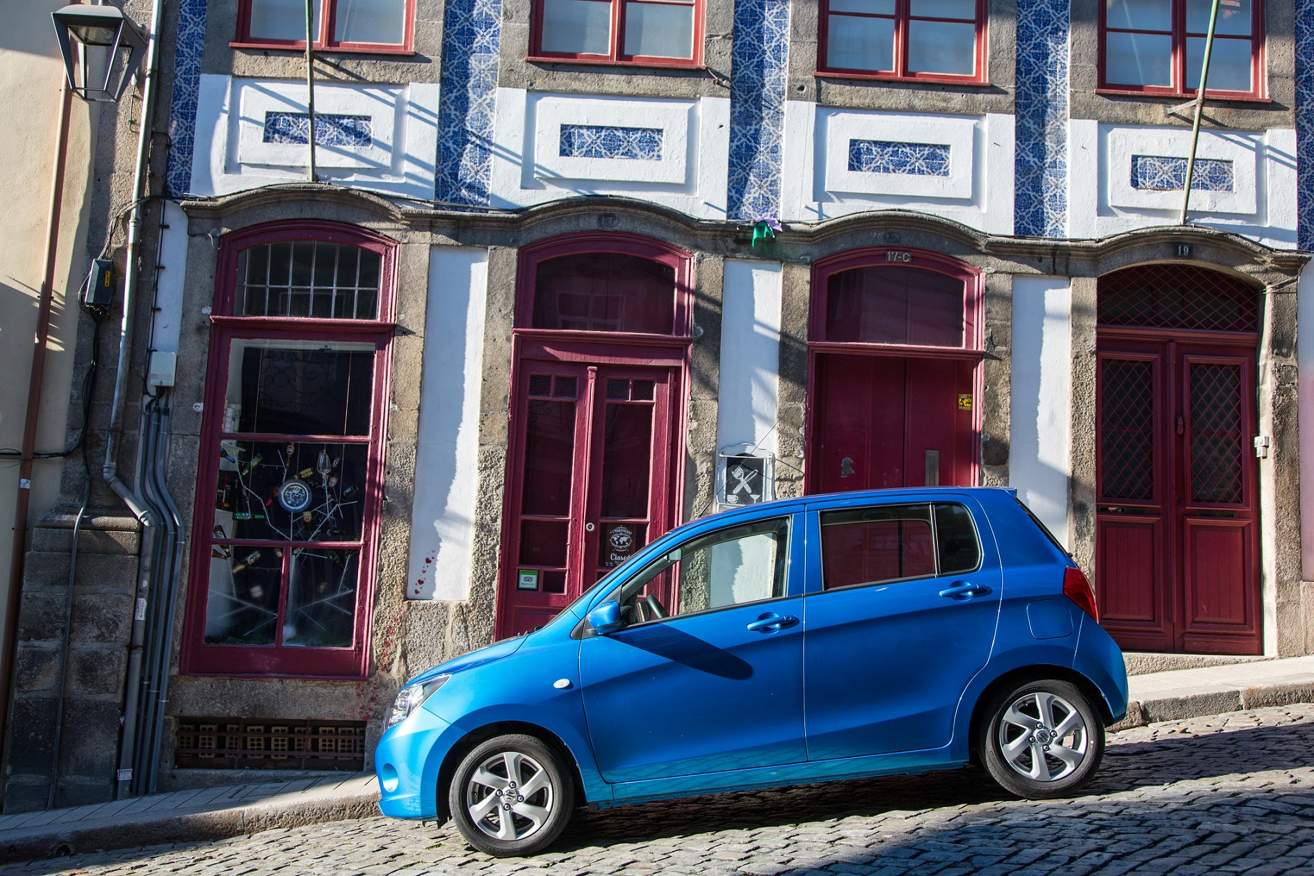 Blaues Auto auf Kopfsteinpflasterstraße vor einem historischen Gebäude mit verzierten Fenstern und blauen Fliesen an der Fassade.