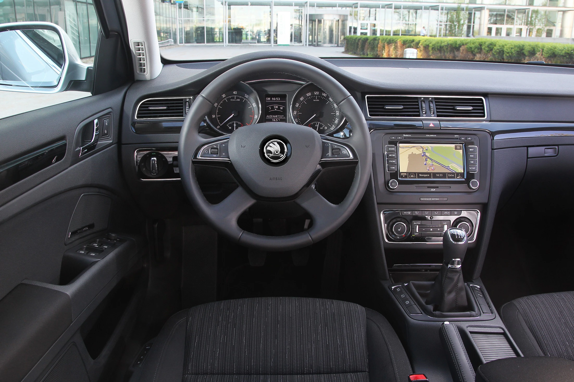Innenraum eines Autos mit Lenkrad, Armaturenbrett mit Tachometer, Infotainment-Bildschirm und Schalthebel. Modernes Design.
