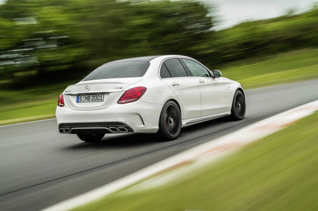 Weißer Mercedes-Benz C-Klasse fährt schnell auf einer Landstraße, umgeben von grüner Landschaft.