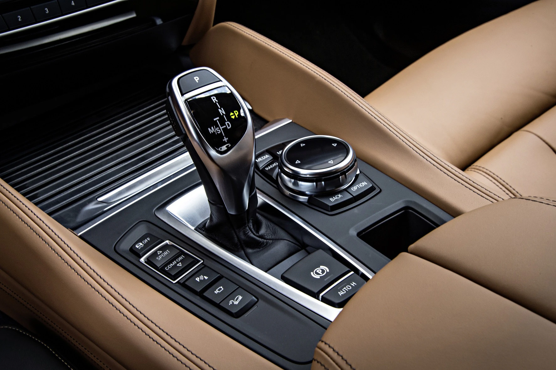 Nahaufnahme einer luxuriösen Autokonsole mit Ledersitzen, einem eleganten Schalthebel und mehreren Bedienknöpfen.
