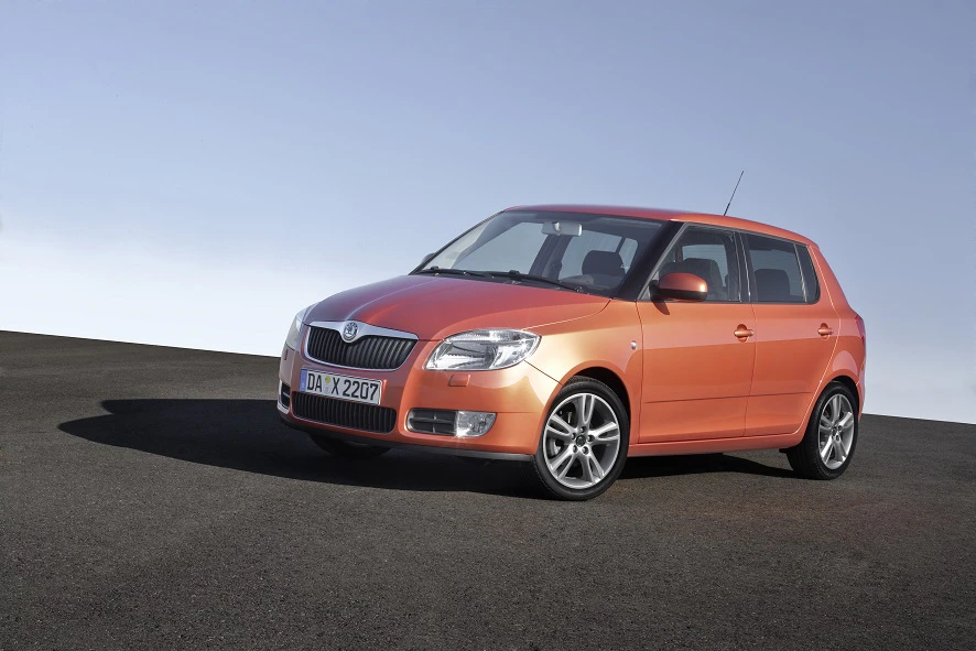 Oranger Skoda Fabia steht auf einer asphaltierten Fläche vor einem blauen Himmel.