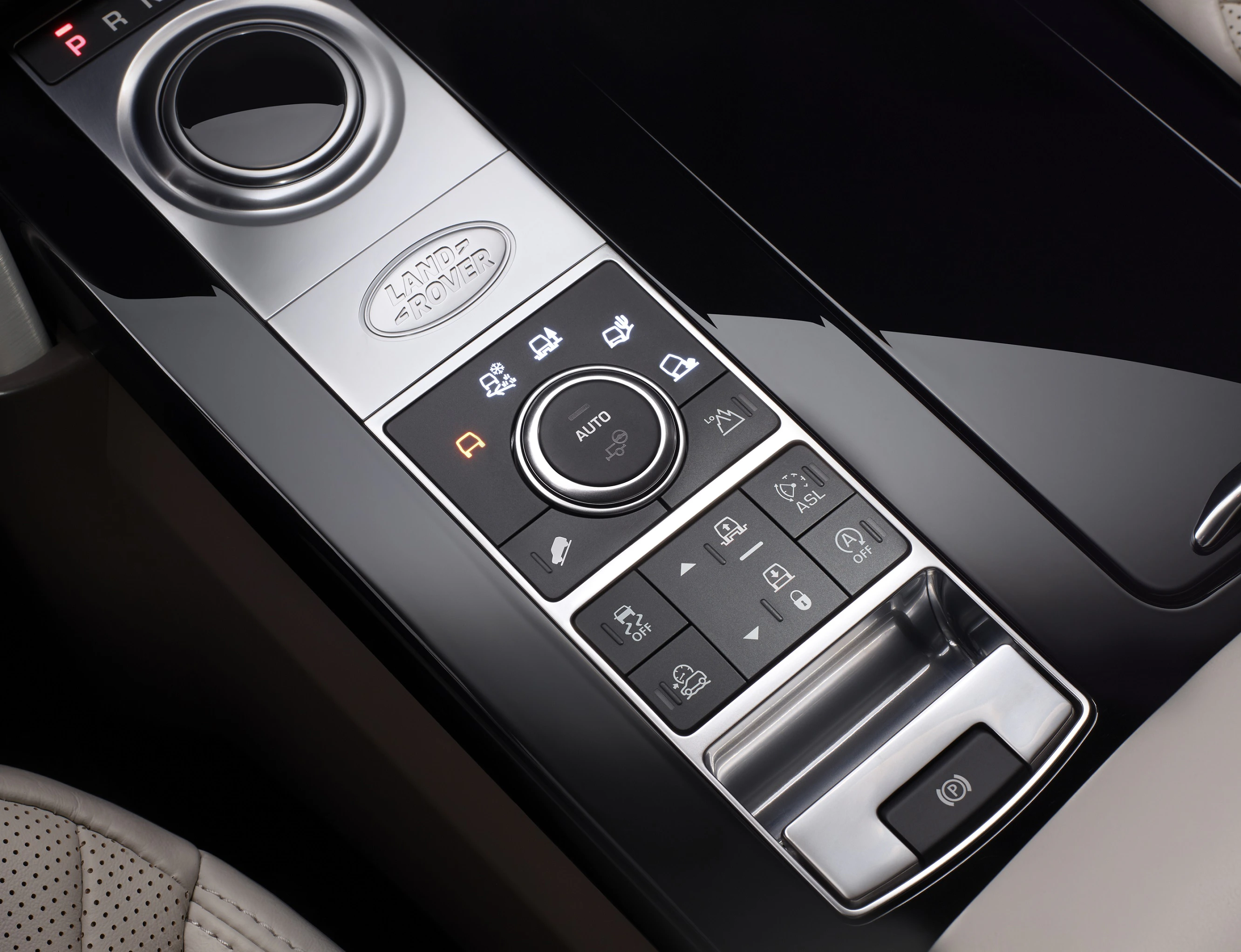Bedienfeld eines Land Rover-Autos mit Drehknopf und verschiedenen Tasten für Fahrzeugfunktionen auf glänzendem schwarzen Hintergrund.