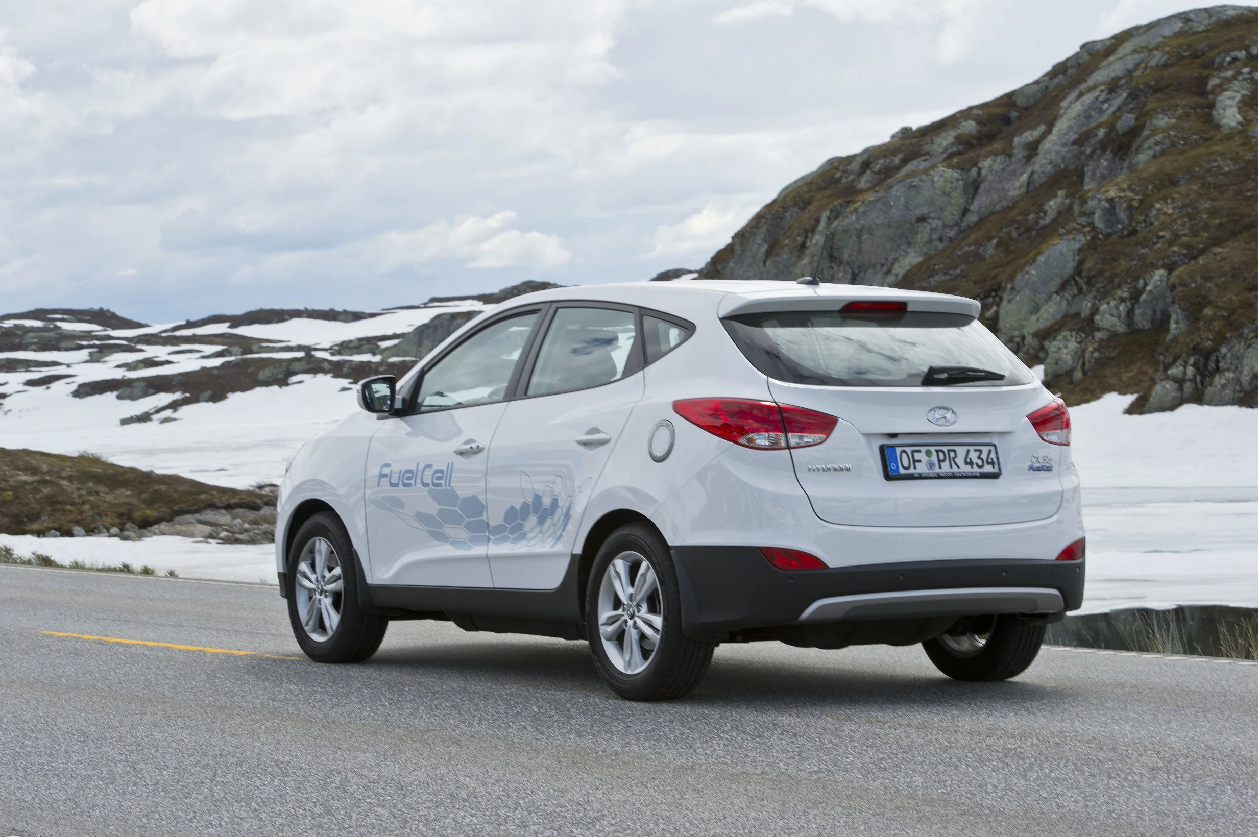 Weißer SUV fährt auf einer Bergstraße mit Schnee und Felsen; Aufschrift "Fuel Cell" an der Seite.