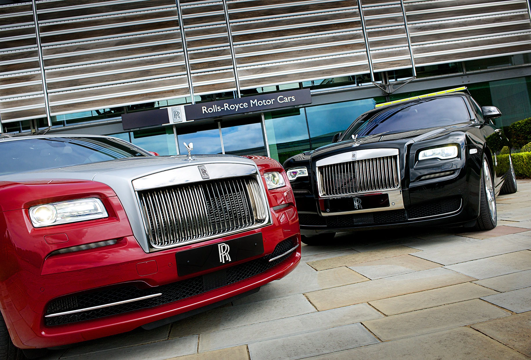 Zwei luxuriöse Rolls-Royce Autos, rot und schwarz, vor dem Rolls-Royce Motor Cars Gebäude geparkt.