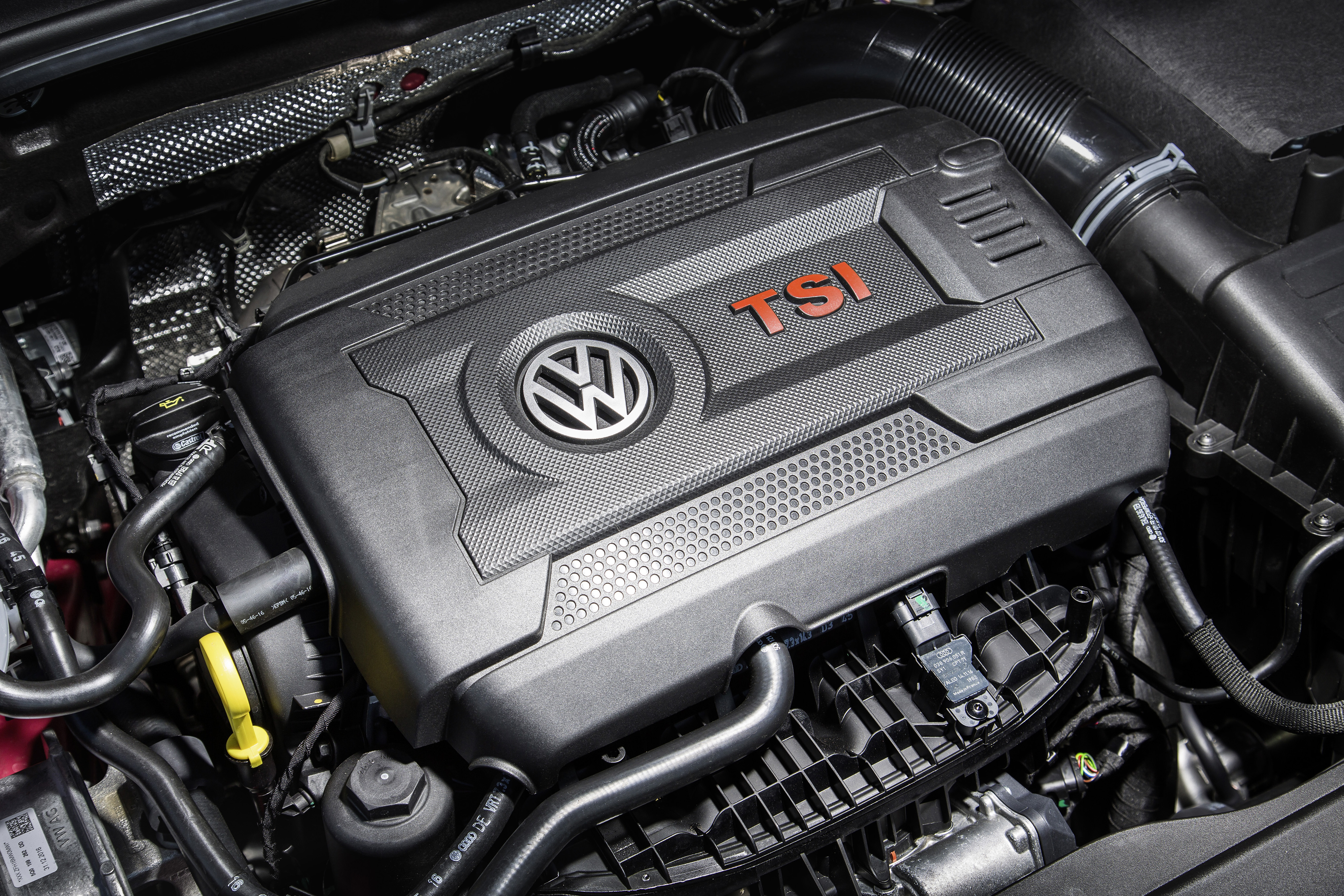 Nahansicht eines Volkswagen TSI-Motors mit schwarzem Gehäuse und roten "TSI"-Buchstaben. Darum befinden sich verschiedene Motorbauteile.