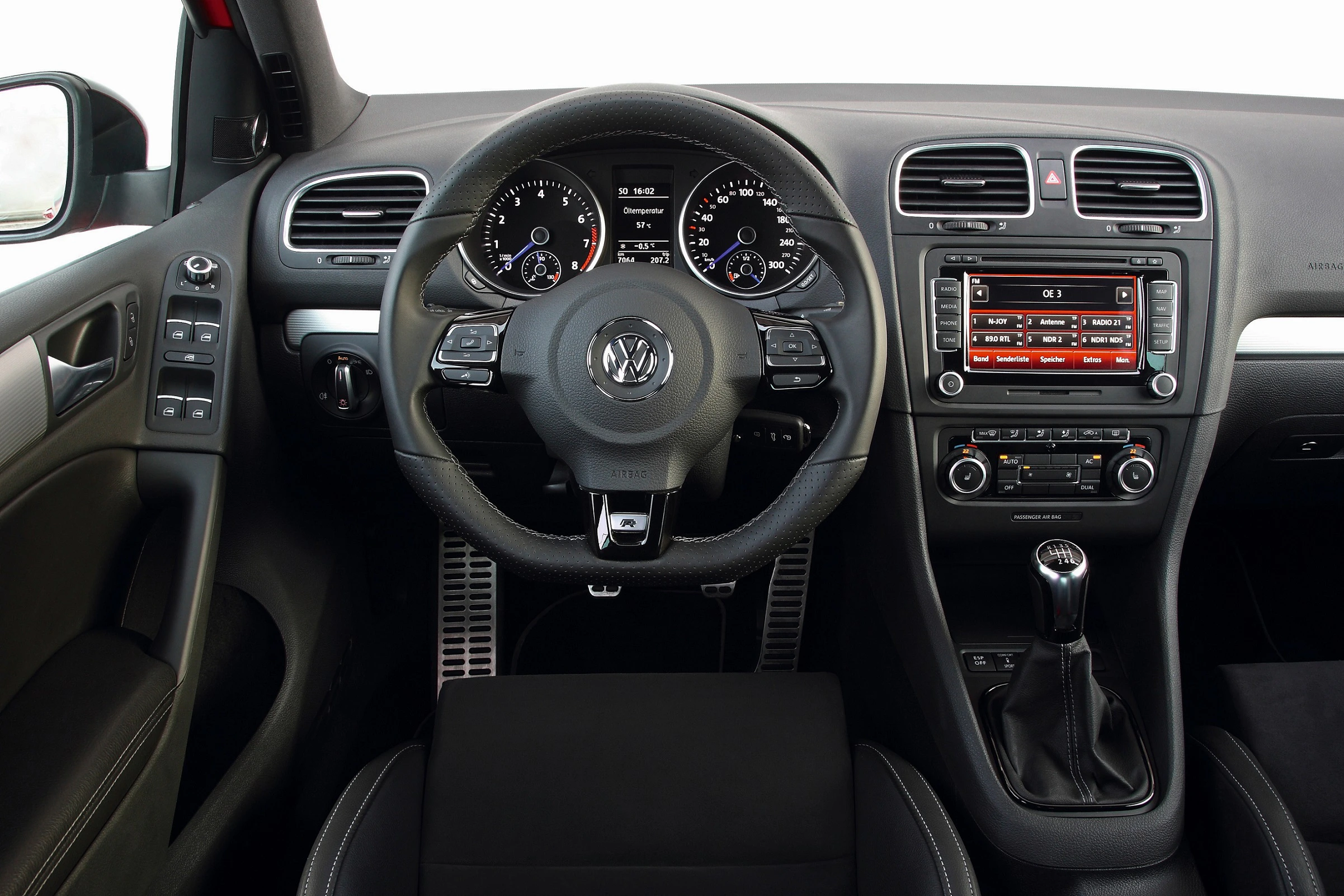 Innenraum eines Autos mit Volkswagen-Logo auf dem Lenkrad, Tachometer, und einem zentralen Infotainment-System mit roten Displays.
