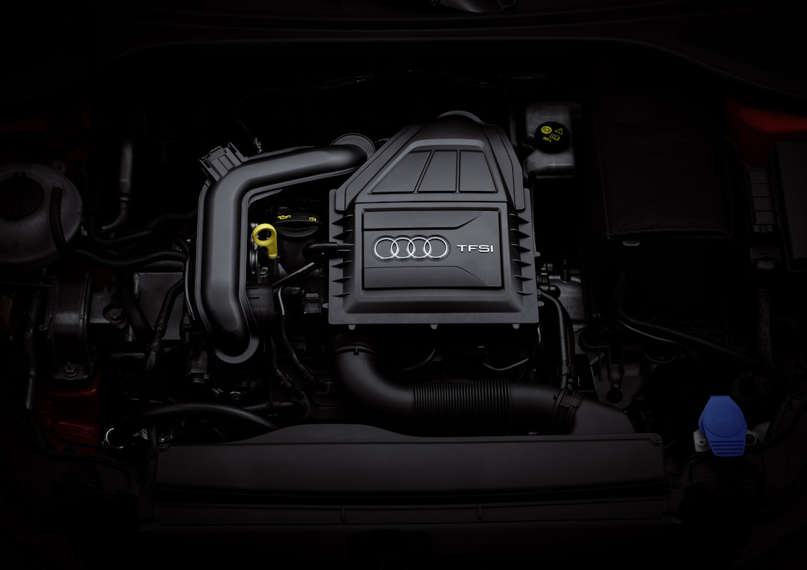 Motorraum eines Autos mit sichtbarem Audi TFSI-Motor, Rohren und farbigen Verschlusskappen.