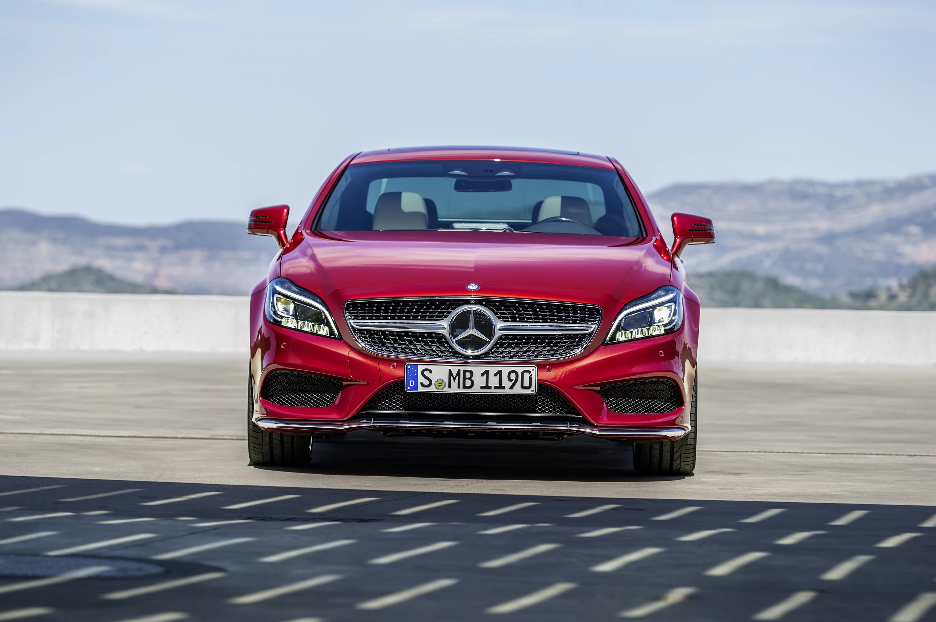 Roter Mercedes-Benz auf einer Straße, Frontansicht. Hintergrund mit Bergen und blauem Himmel.