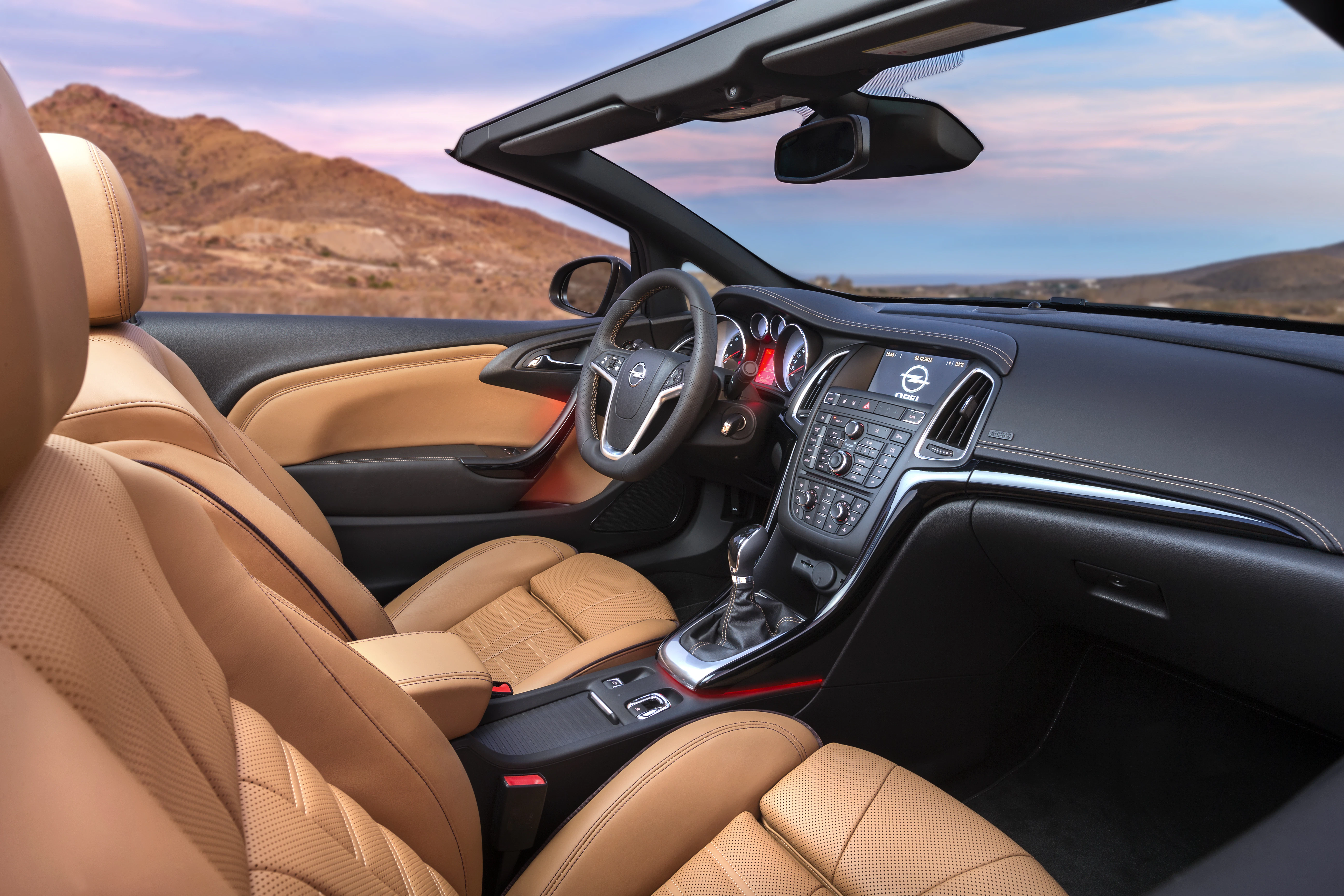 Innenraum eines Cabriolets mit beigen Ledersitzen und modernen Armaturen, parkend vor einer Wüstenlandschaft bei Sonnenuntergang.