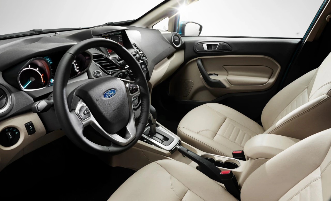 Innenraum eines Autos mit beigen Ledersitzen, einem Lenkrad mit Ford-Logo und einem zentralen Bildschirm auf dem Armaturenbrett.