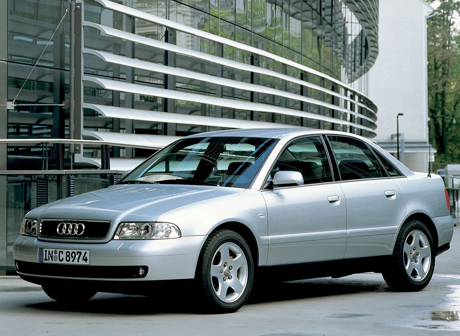 Silberner Audi A4 Limousine steht auf einer Straße vor einem modernen Gebäude mit Glasfassade.