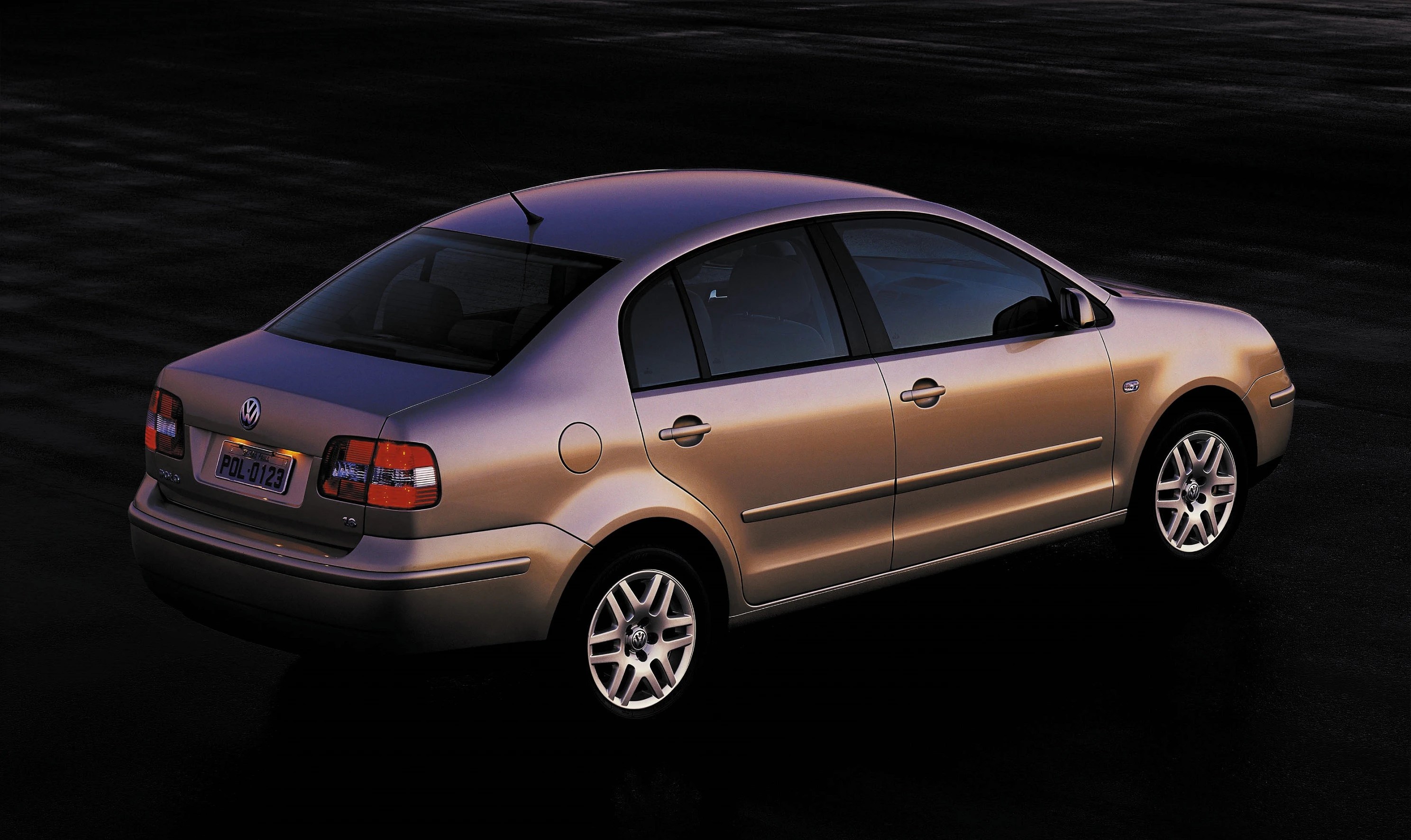 Silberner Volkswagen Polo sedan auf dunklem Hintergrund, von hinten links fotografiert, mit glänzendem Lack und markanten Rückleuchten.