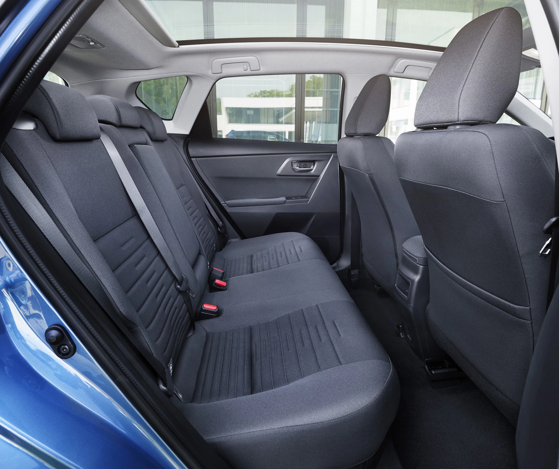 Innenraum eines Autos mit blauen Stoffpolstern, Rücksitze und Vordersitze von der Seite sichtbar, klarer Blick auf Fenster und Autotür.