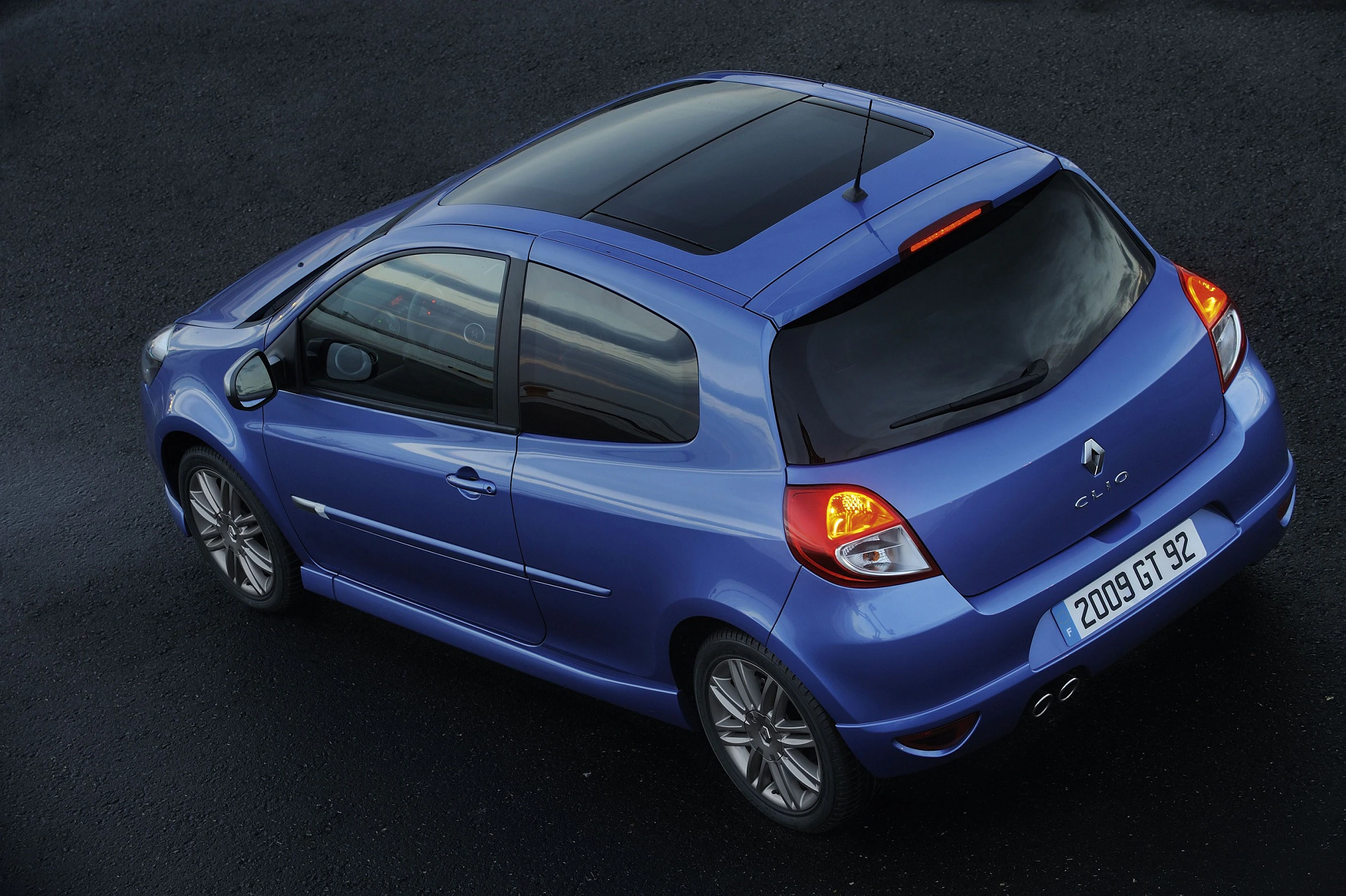 Blauer Renault Clio von schräg oben fotografiert, mit dunklem Dach und 2008er Nummernschild, auf einer dunklen Asphaltfläche geparkt.