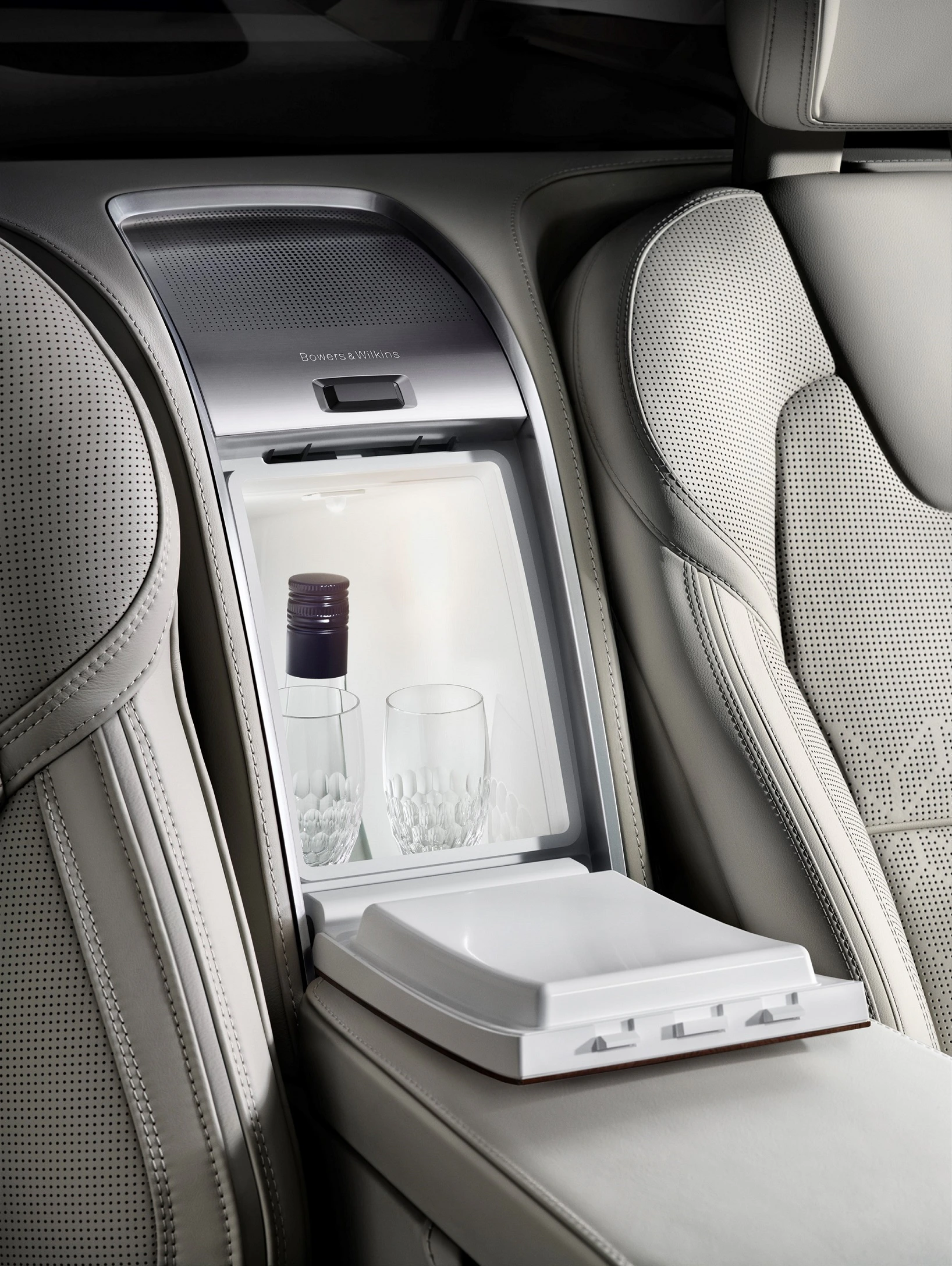 Kühlschrank im Fond eines Luxusautos mit zwei Kristallgläsern und einer Weinflasche. Umgeben von heller Lederausstattung.