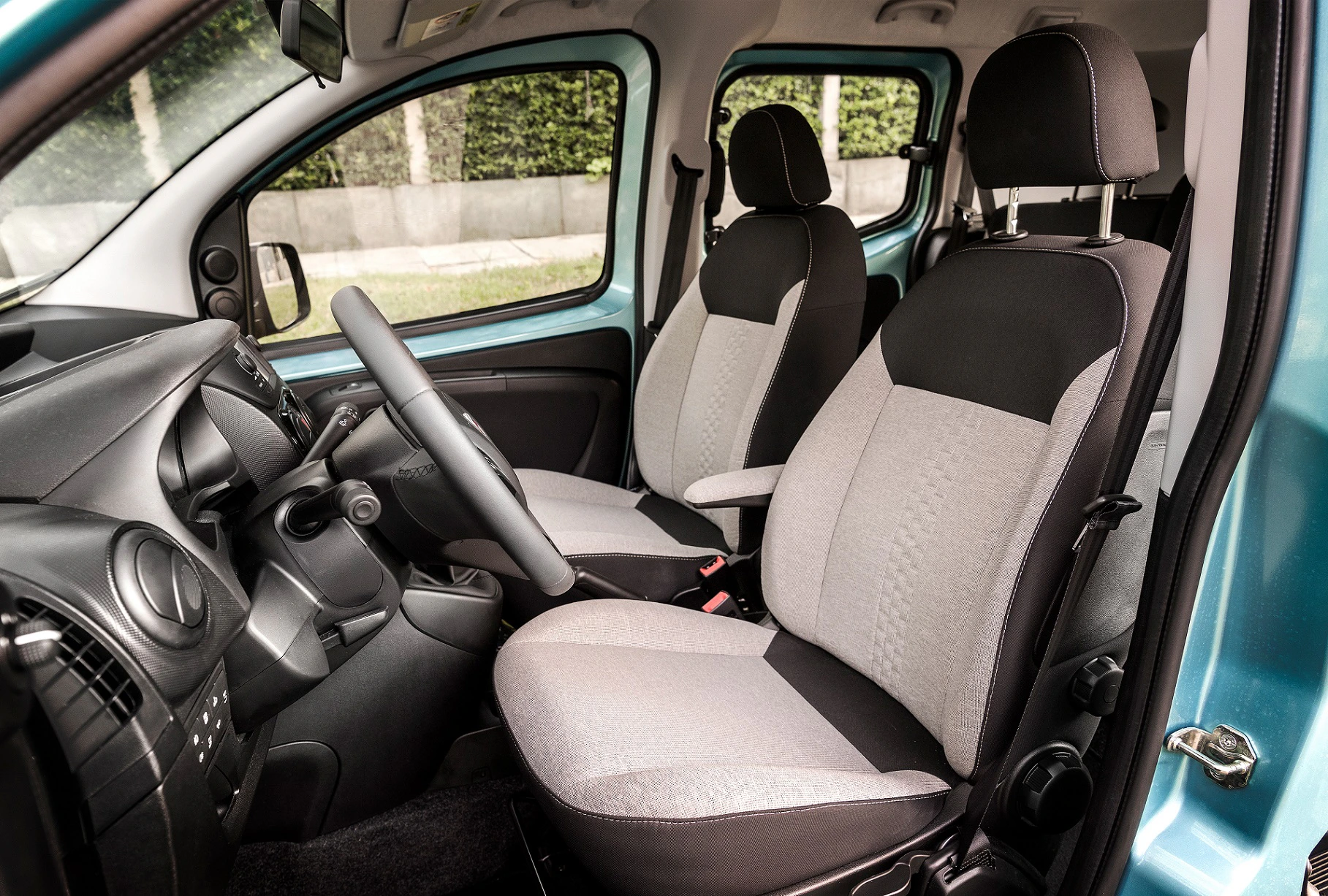Innenraum eines Autos mit grauen und schwarzen Stoffpolstern, zwei vorderen Sitzen, Lenkrad und Instrumententafel, Blick von der rechten Seite.
