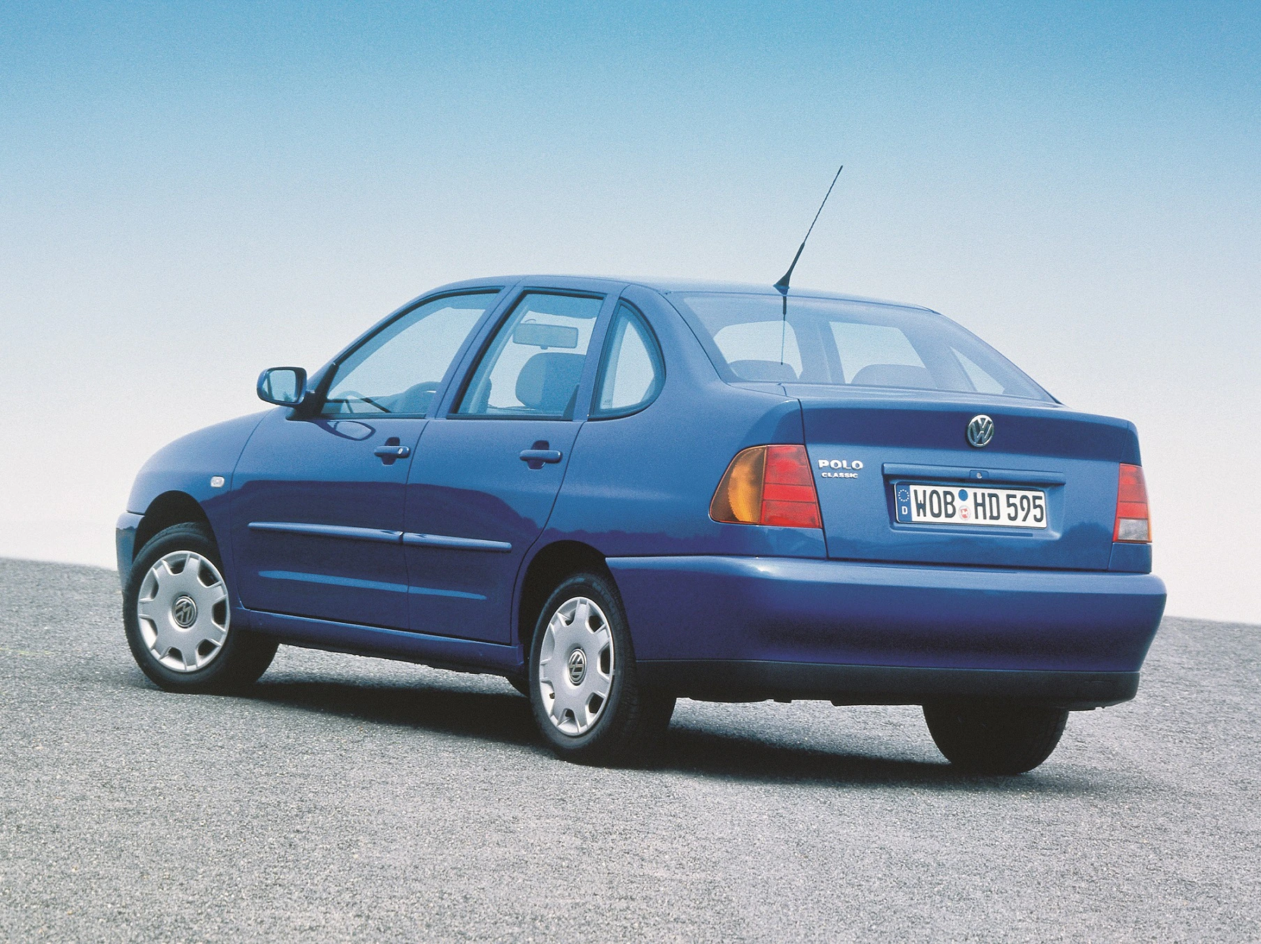 Blaues Volkswagen Polo Classic-Modell auf einem Parkplatz von hinten fotografiert, bei klarem Himmel.