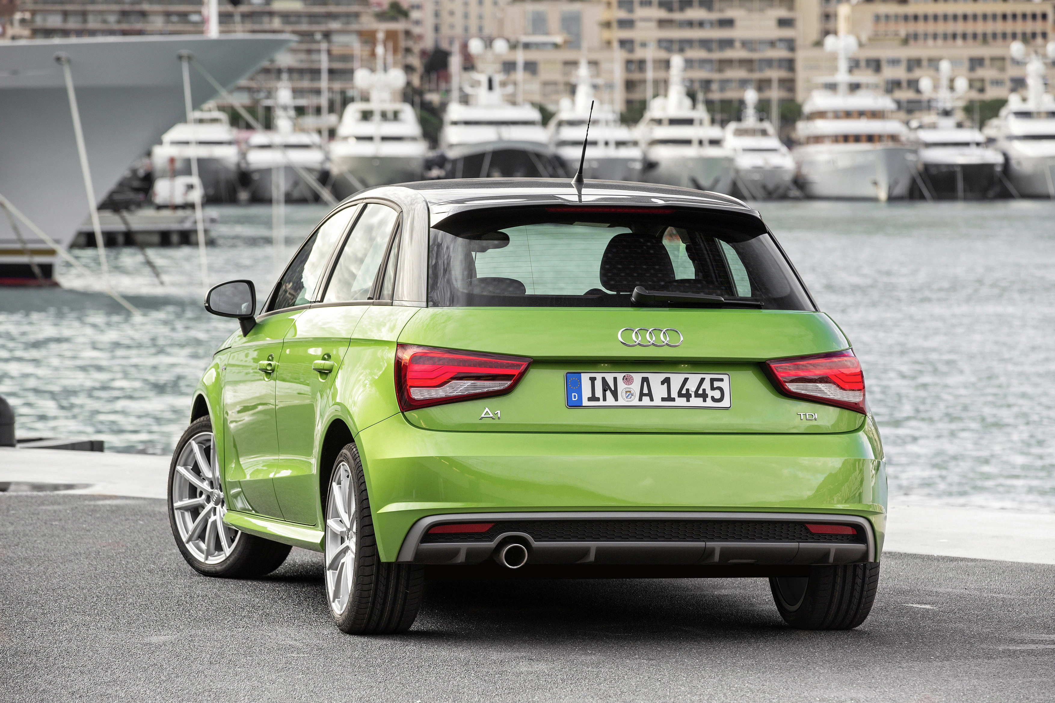 Grüner Audi A1 parkt am Hafen, im Hintergrund Yachten und Stadtansicht. Elegante, moderne Kulisse mit Wasser und Booten.