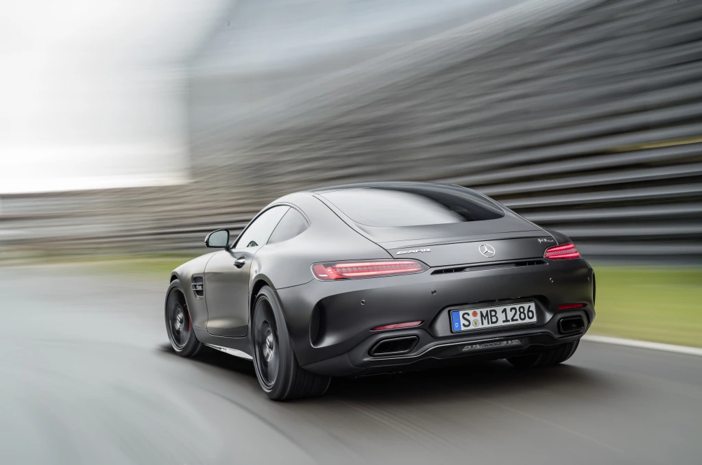 Sportlicher, grauer Mercedes-AMG GT fährt dynamisch auf einer nassen Straße, umgeben von verschwommenem Hintergrund.