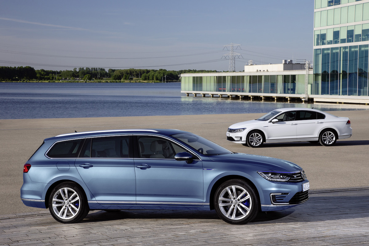 Zwei geparkte Autos am Wasser; ein blauer Kombi im Vordergrund und ein weißer Wagen im Hintergrund, mit einem modernen Gebäude rechts.