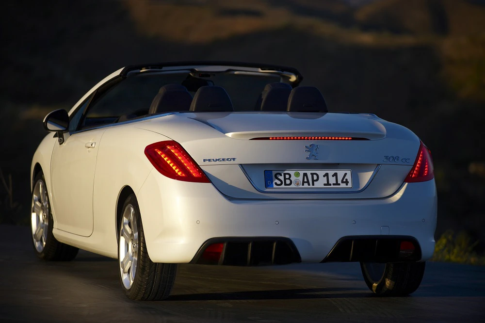 Weißer Peugeot Cabrio mit geöffnetem Verdeck, Heckansicht bei Sonnenuntergang. Nummernschild „SB AP 114“.