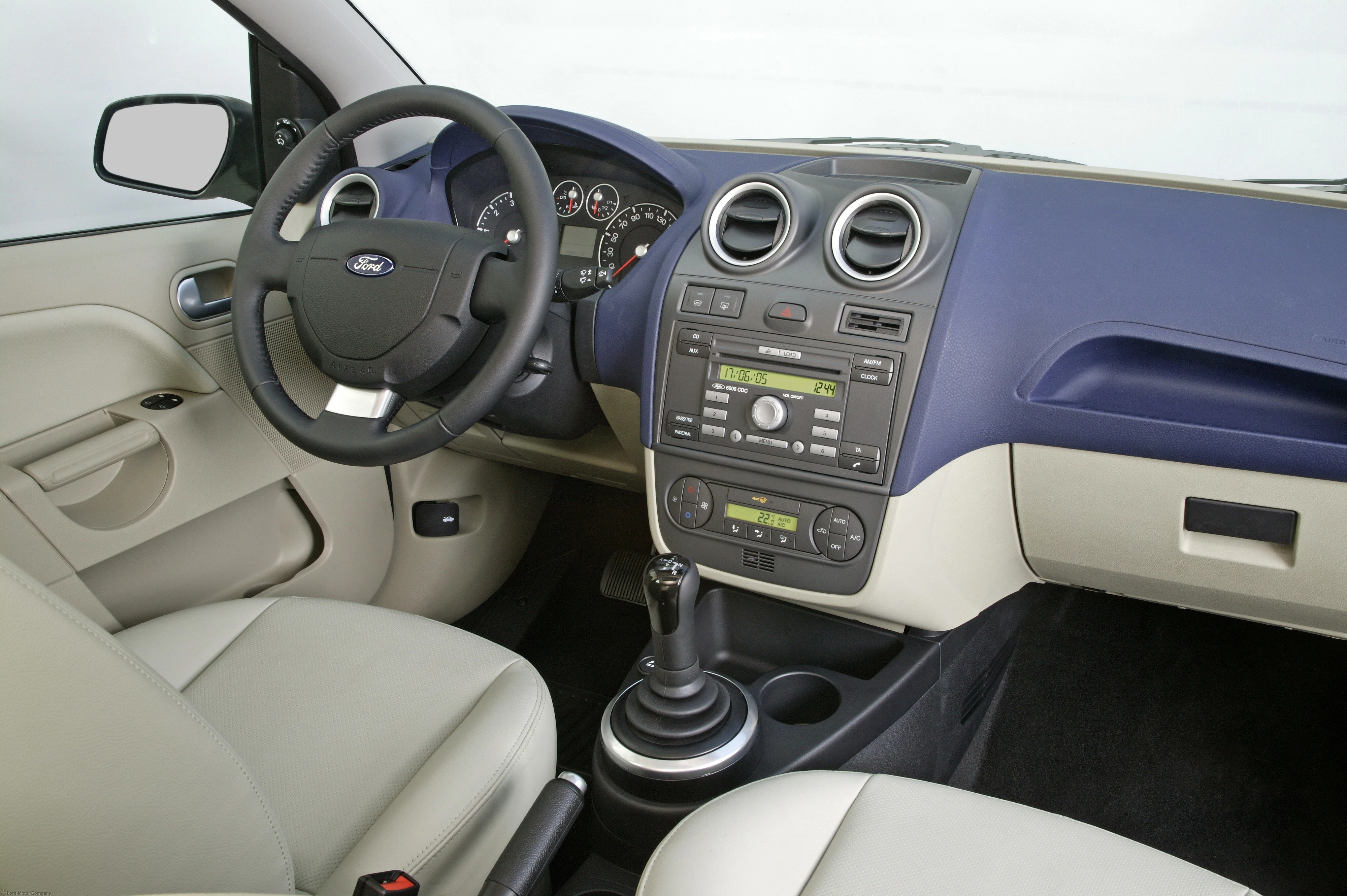 Innenraum eines Autos. Sicht auf das Lenkrad, Armaturenbrett mit Radio und Klimaanlage. Helle Ledersitze, manuelle Gangschaltung.