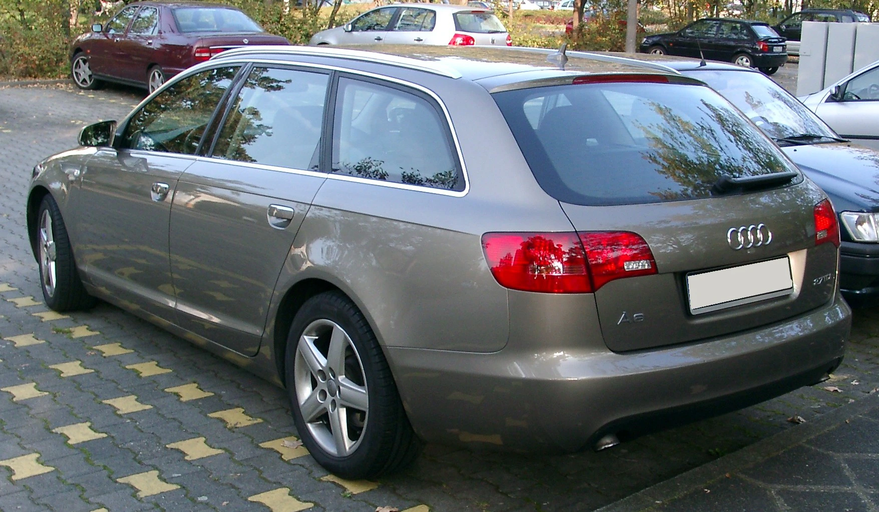 Grauer Audi Kombi auf einem Parkplatz, umgeben von Autos und Bäumen im Hintergrund.