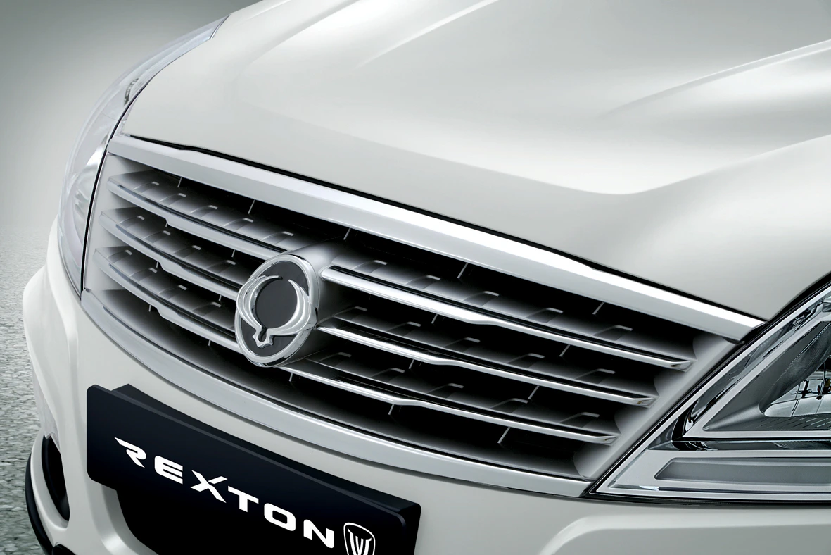 Nahaufnahme eines weißen SUV mit markantem Kühlergrill und Logo. Der Markenname "REXTON" ist auf einem Schild vorne sichtbar.