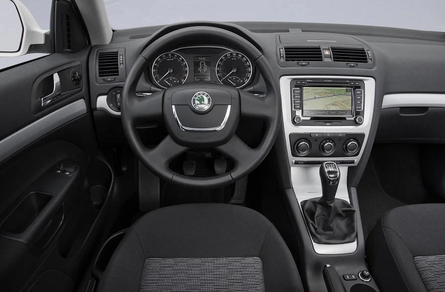 Innenraum eines Autos mit einem Lenkrad, einem Armaturenbrett mit Tachometern und einem Navigationsbildschirm, sowie einem Schaltknüppel.
