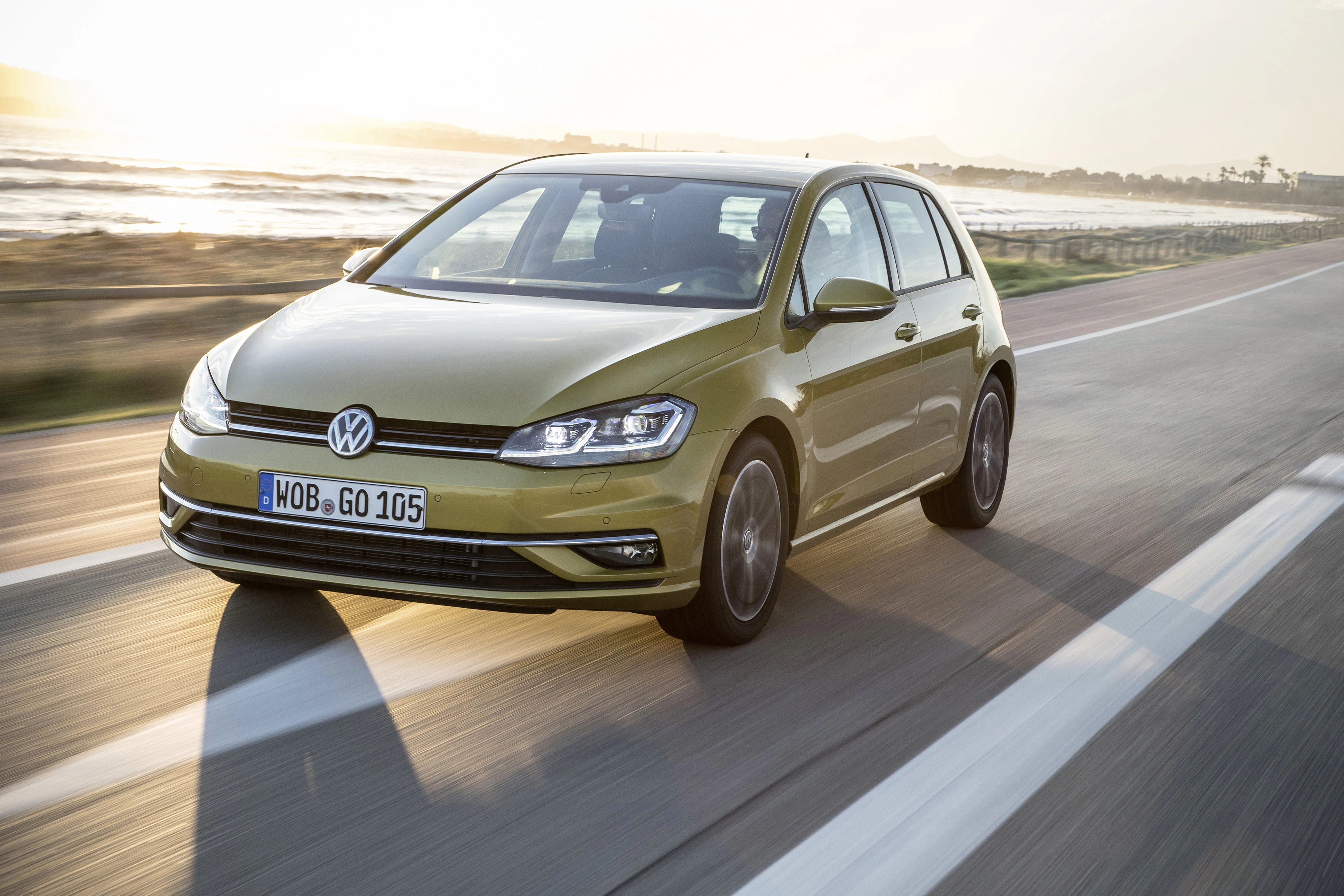 Grüner Volkswagen Golf fährt auf einer Straße entlang der Küste bei Sonnenuntergang.